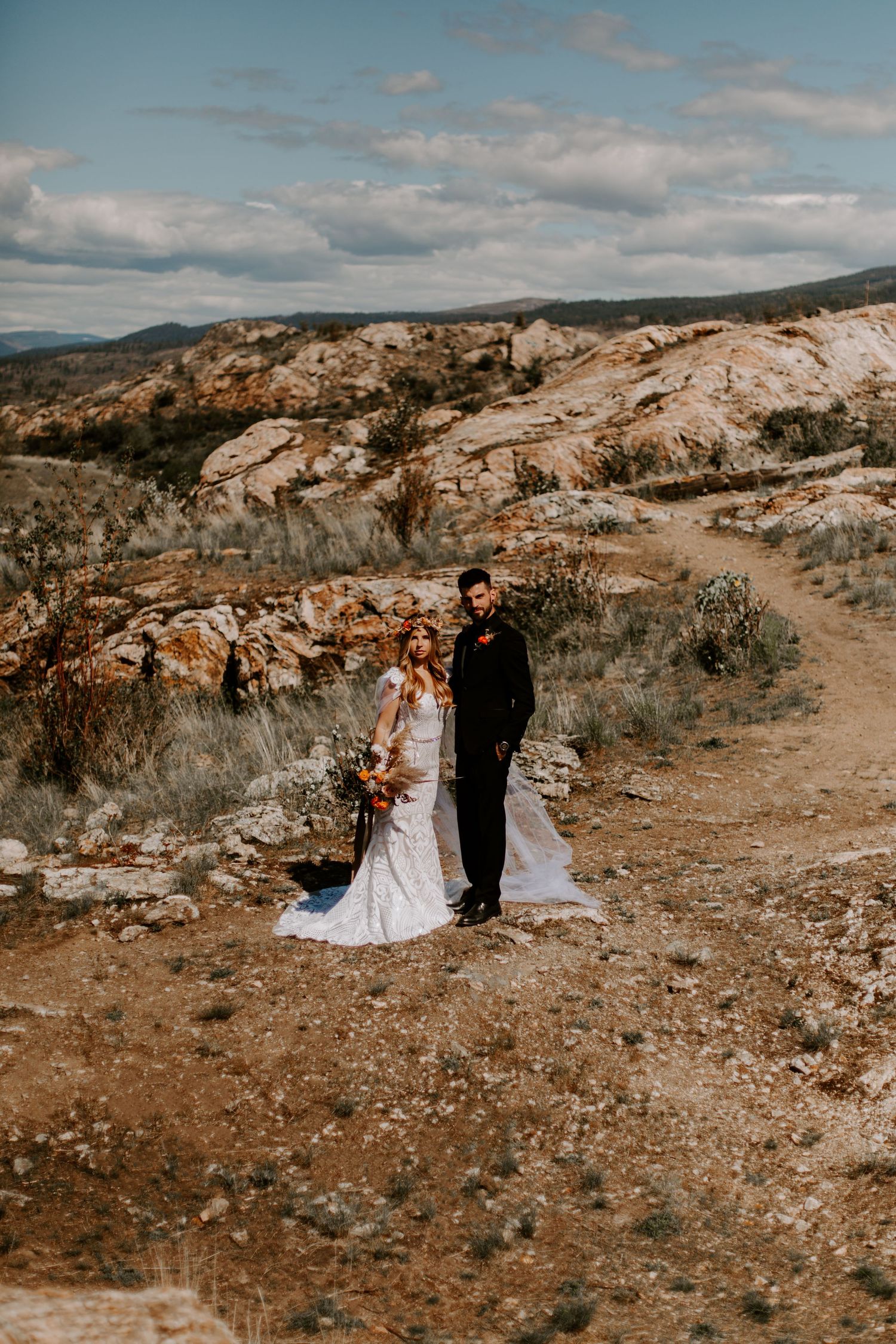 Scenic desert mountain wedding photography session with dramatic rocky landscape and cloudy skies.