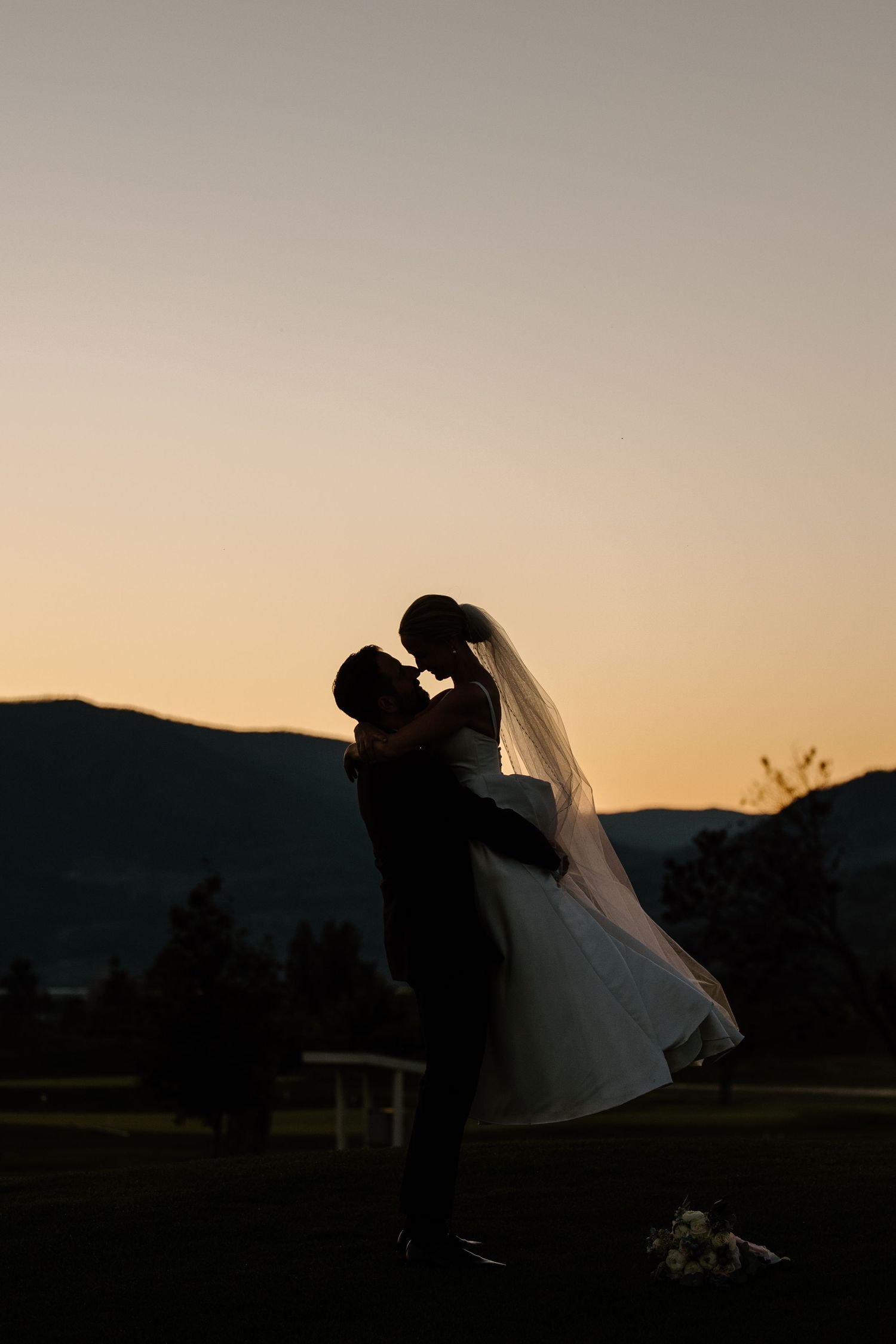 A romantic silhouette of newlyweds embracing against a sunset backdrop with mountains in the distance.
