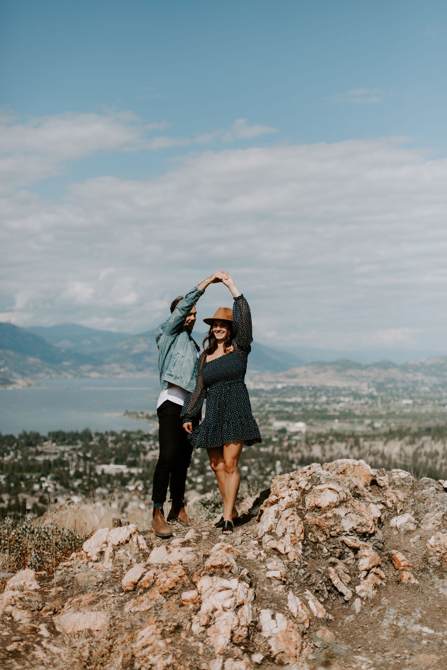 A couple dances together on a rocky overlook with mountain and lake views.