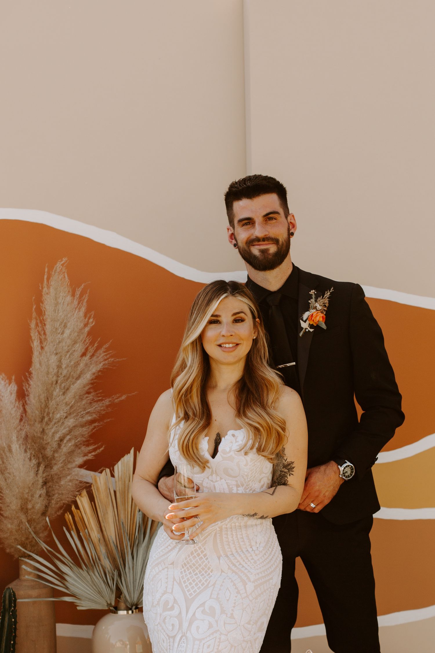 Modern wedding portraits with orange abstract wall backdrop and pampas grass decor.