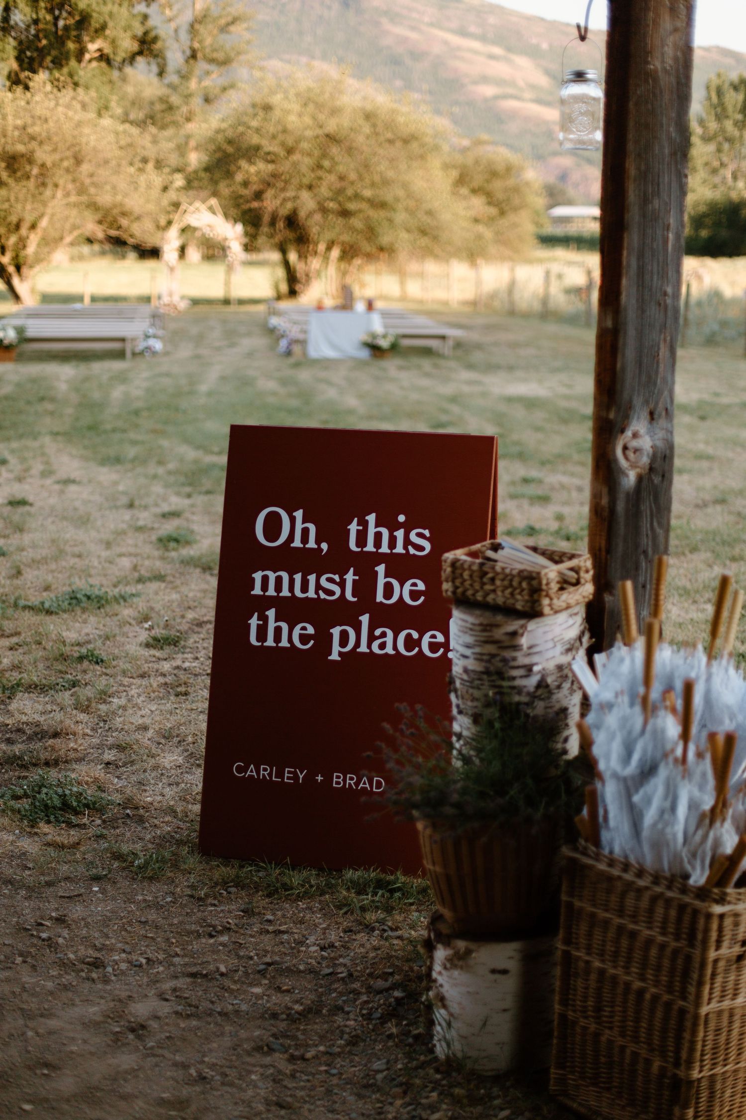 A burgundy wedding sign reading 'Oh, this must be the place' displayed against a rustic birch post.
