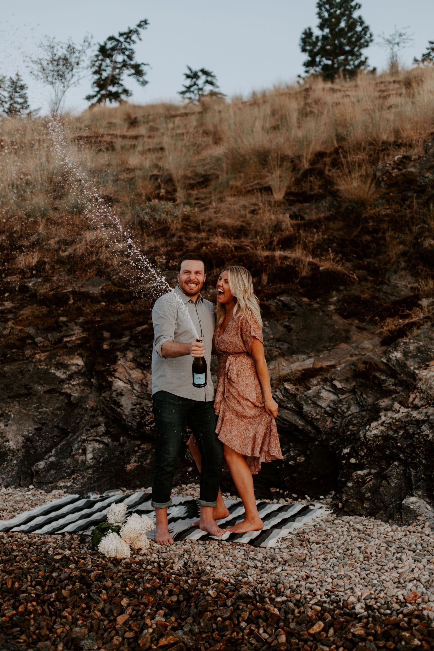 A couple sits together on a picnic blanket during a romantic outdoor photoshoot.