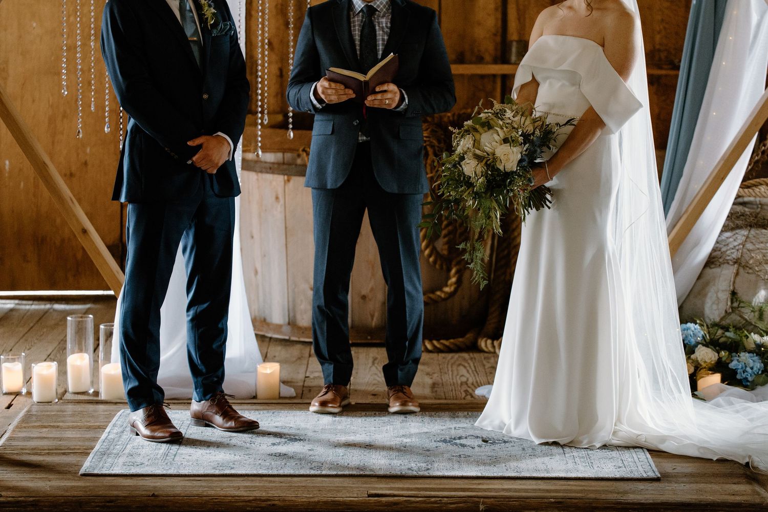 Wedding ceremony takes place in rustic barn venue decorated with white fabric draping from wooden beams.