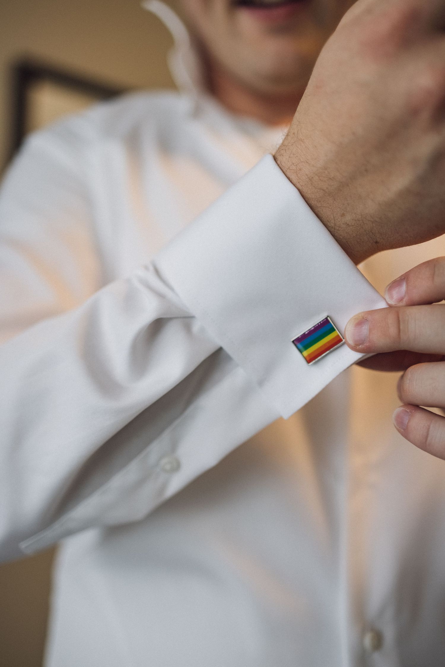 Close-up of rainbow pride flag cufflink on white dress shirt sleeve.