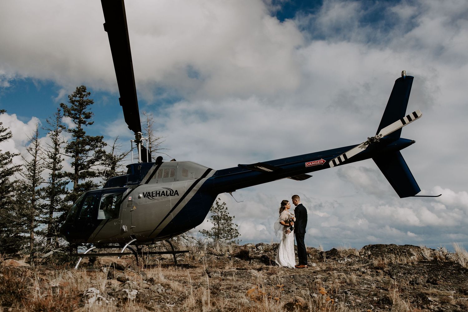 Wedding couple silhouetted against dramatic sky with military helicopter overhead.