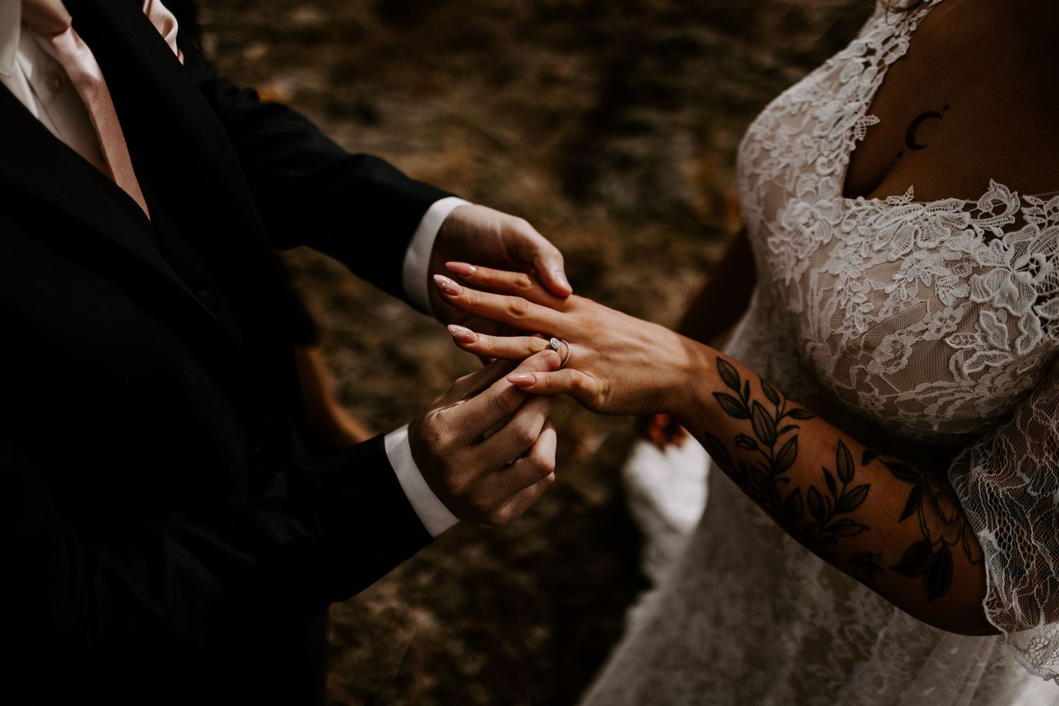 Close-up shot of ring exchange during wedding ceremony with lace dress details.