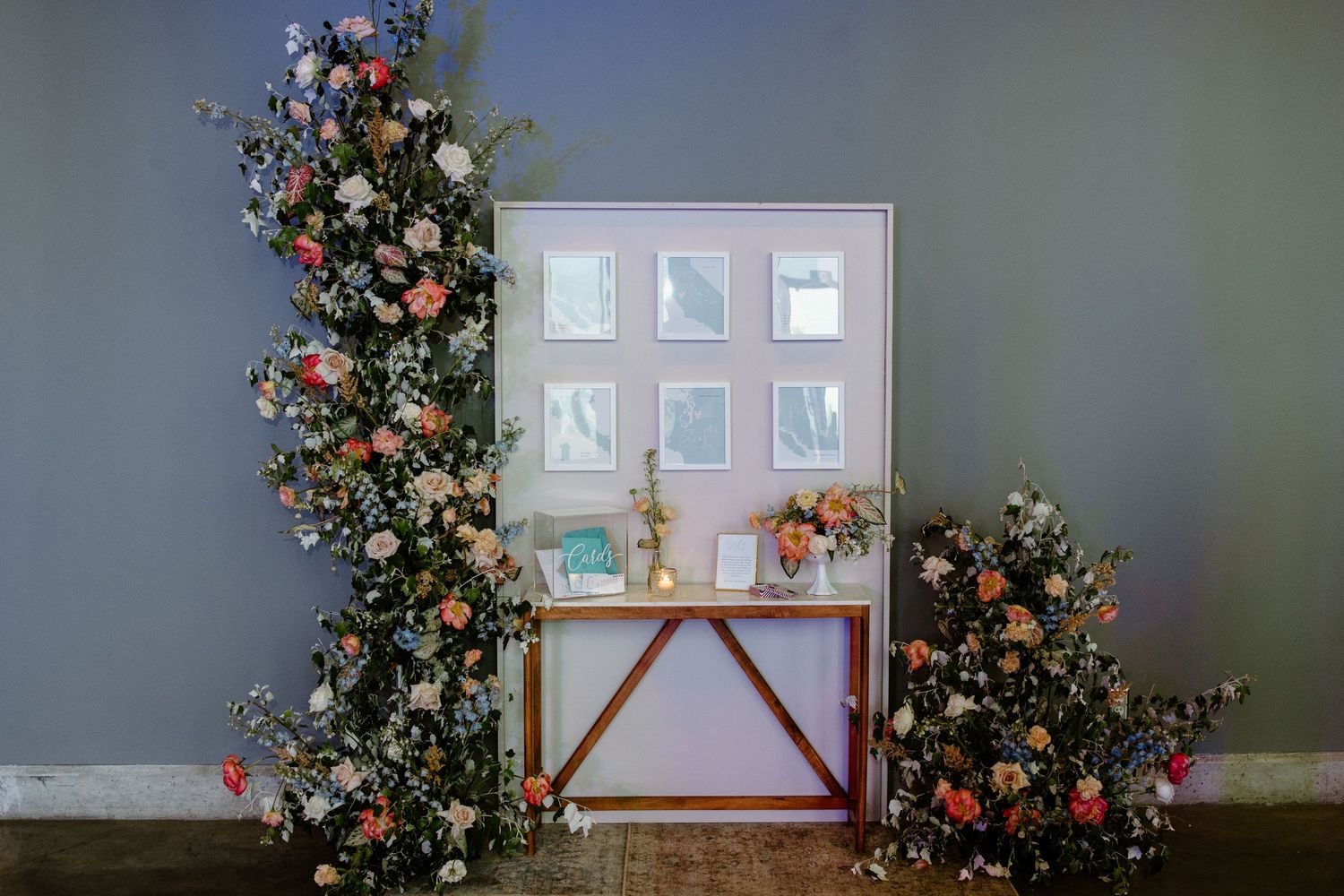 Elegant floral wedding display with colorful blooms flanking a white framed seating chart on a gold console table.