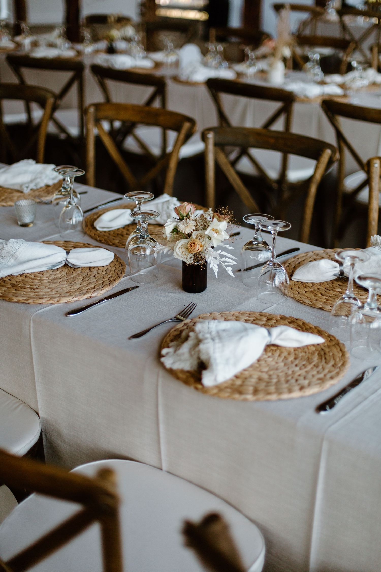 Place settings at a wedding reception feature white tablecloths, woven placemats, and elegant glassware.