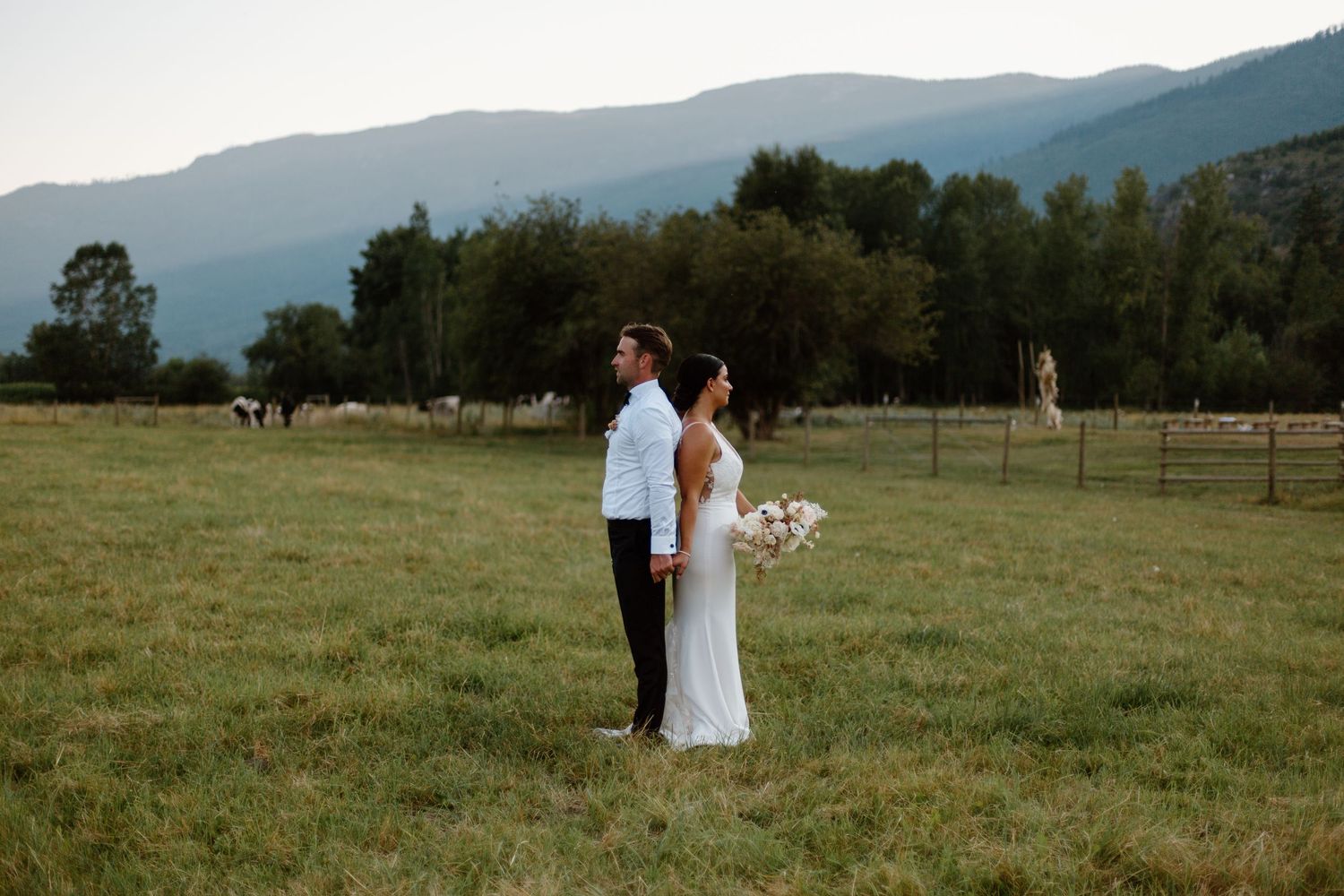 A couple stands together in a scenic mountain meadow during their outdoor wedding ceremony.