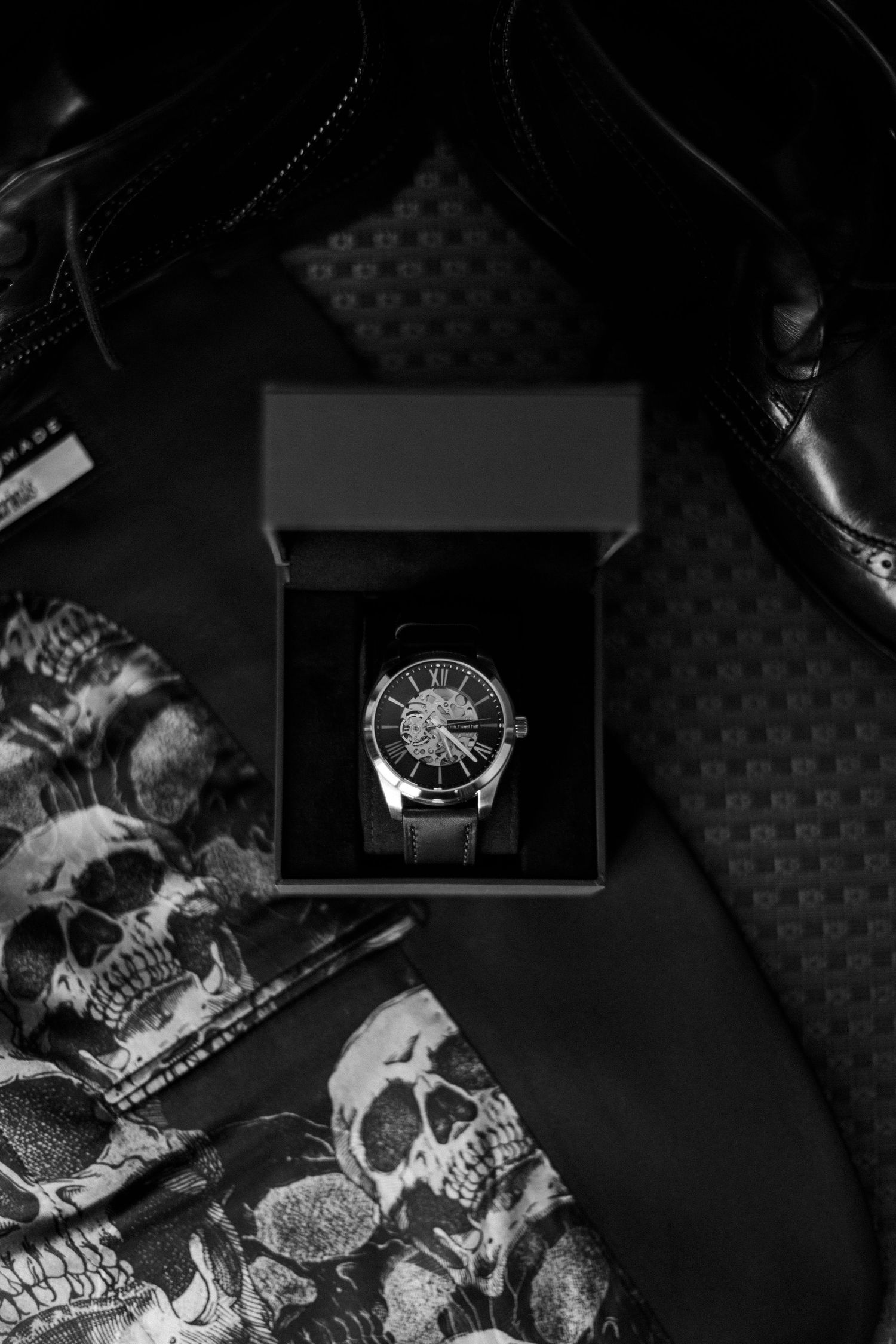 Black and white detail shots of luxury watches and jewelry arranged on dark textured surface.