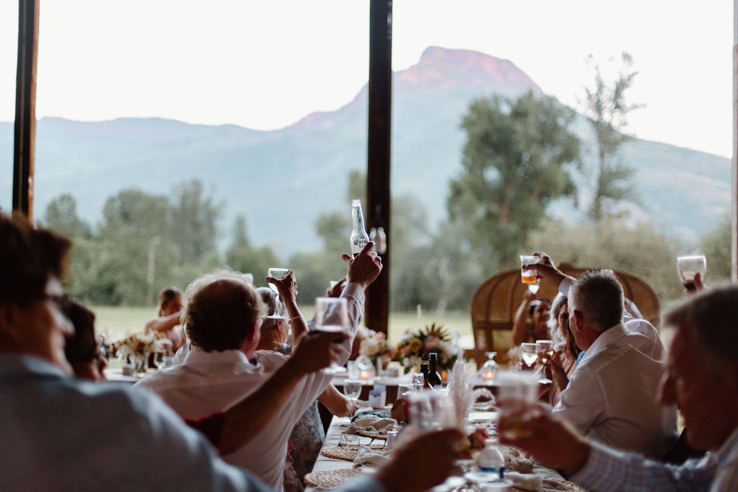 Wedding guests raise their glasses in a toast during an outdoor reception with mountain views.
