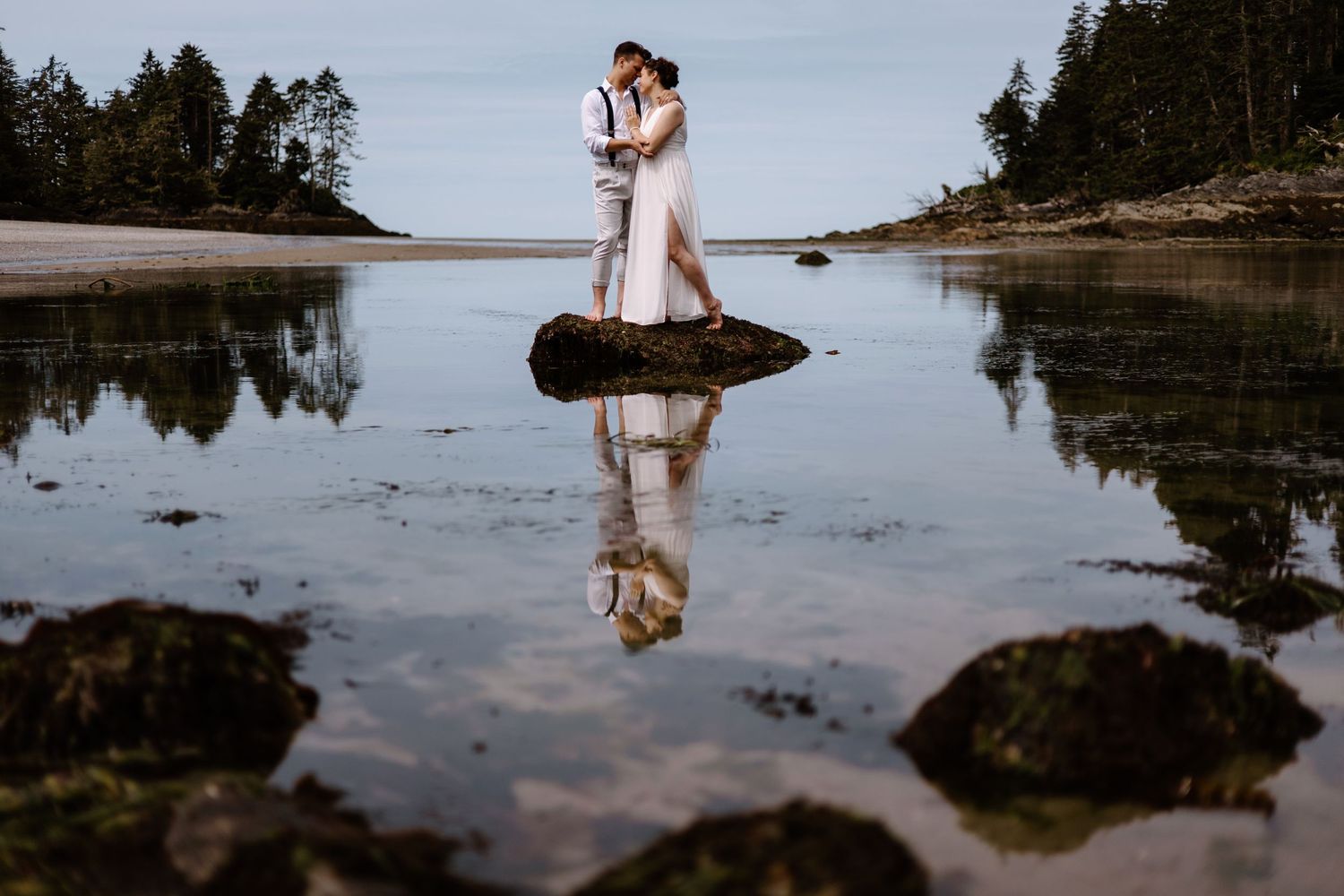 Wedding couple's reflection captured in coastal tide pools at dusk.