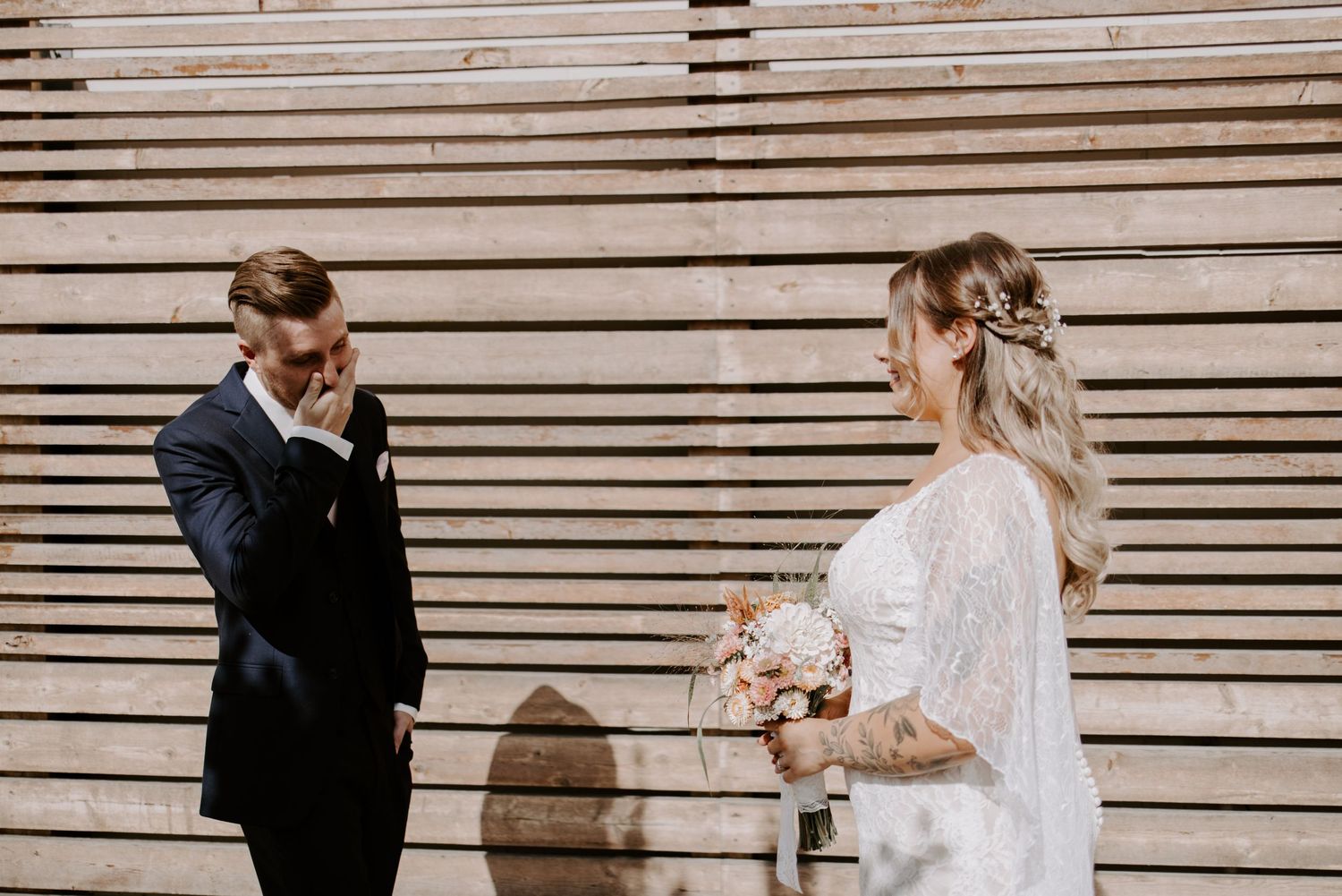 A couple shares an emotional moment during their wedding ceremony against a wooden slatted wall.