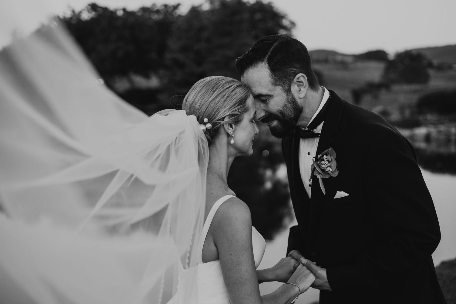 Black and white wedding photo of bride and groom smiling together, veil flowing in wind.