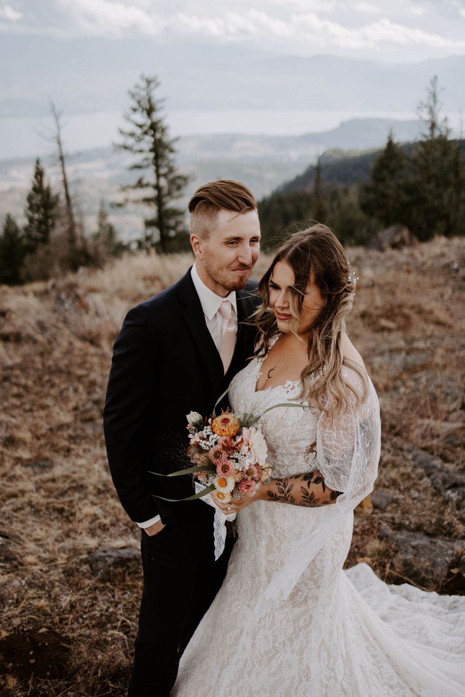 Wedding couple laughs together while holding autumn bouquet on mountainous terrain.