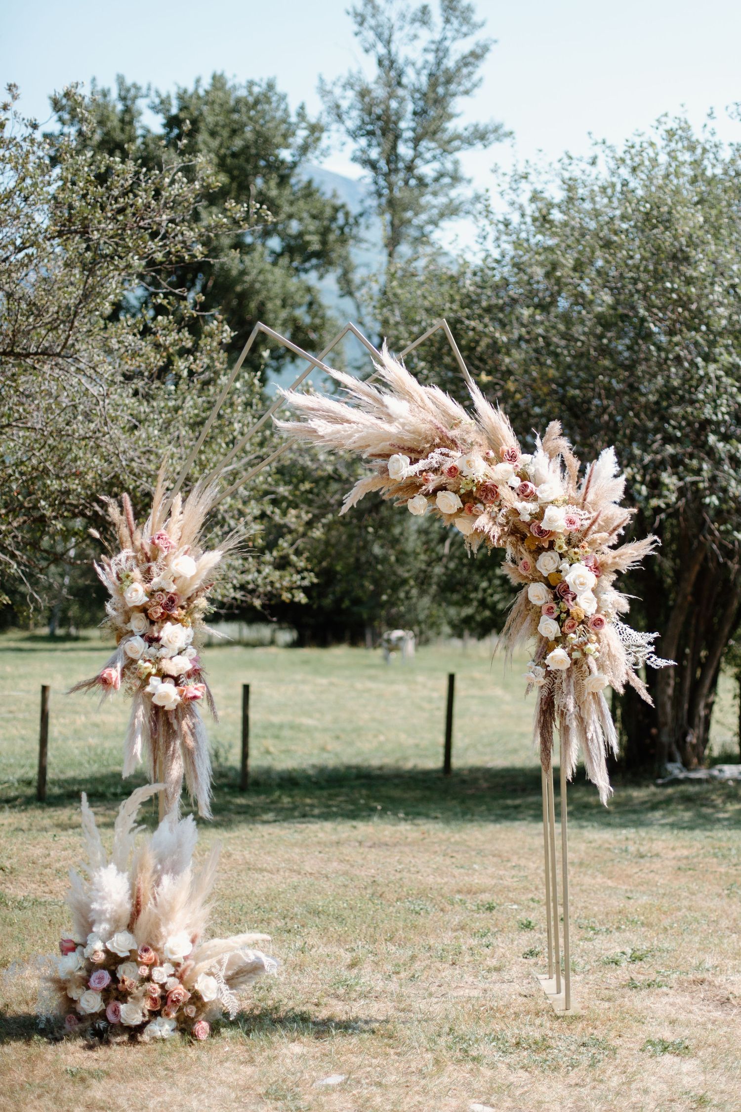 Outdoor wedding ceremony setup with pampas grass and floral arrangements lining a rustic path.