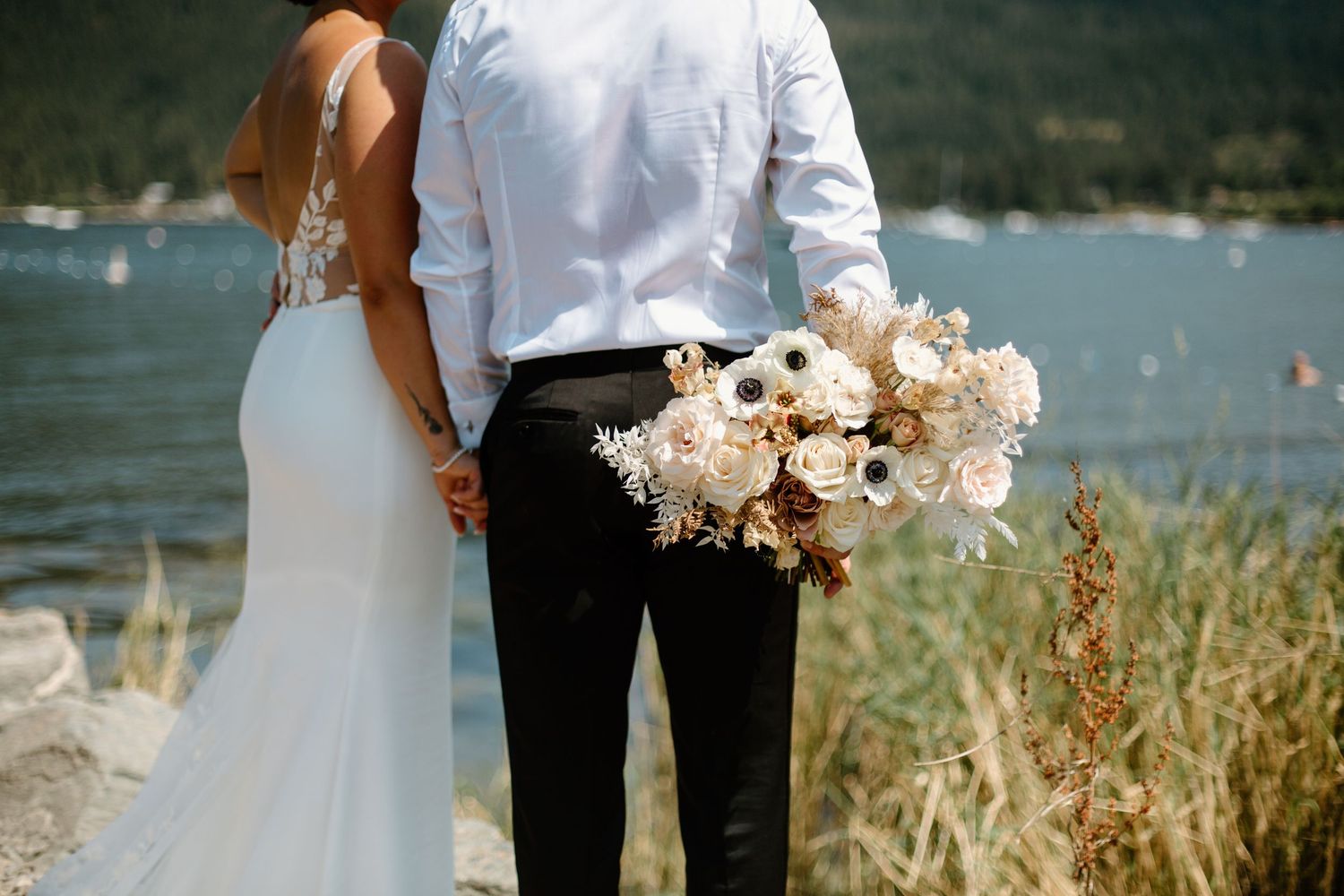 Romantic lakeside moment with bouquet of white flowers and mountain backdrop.