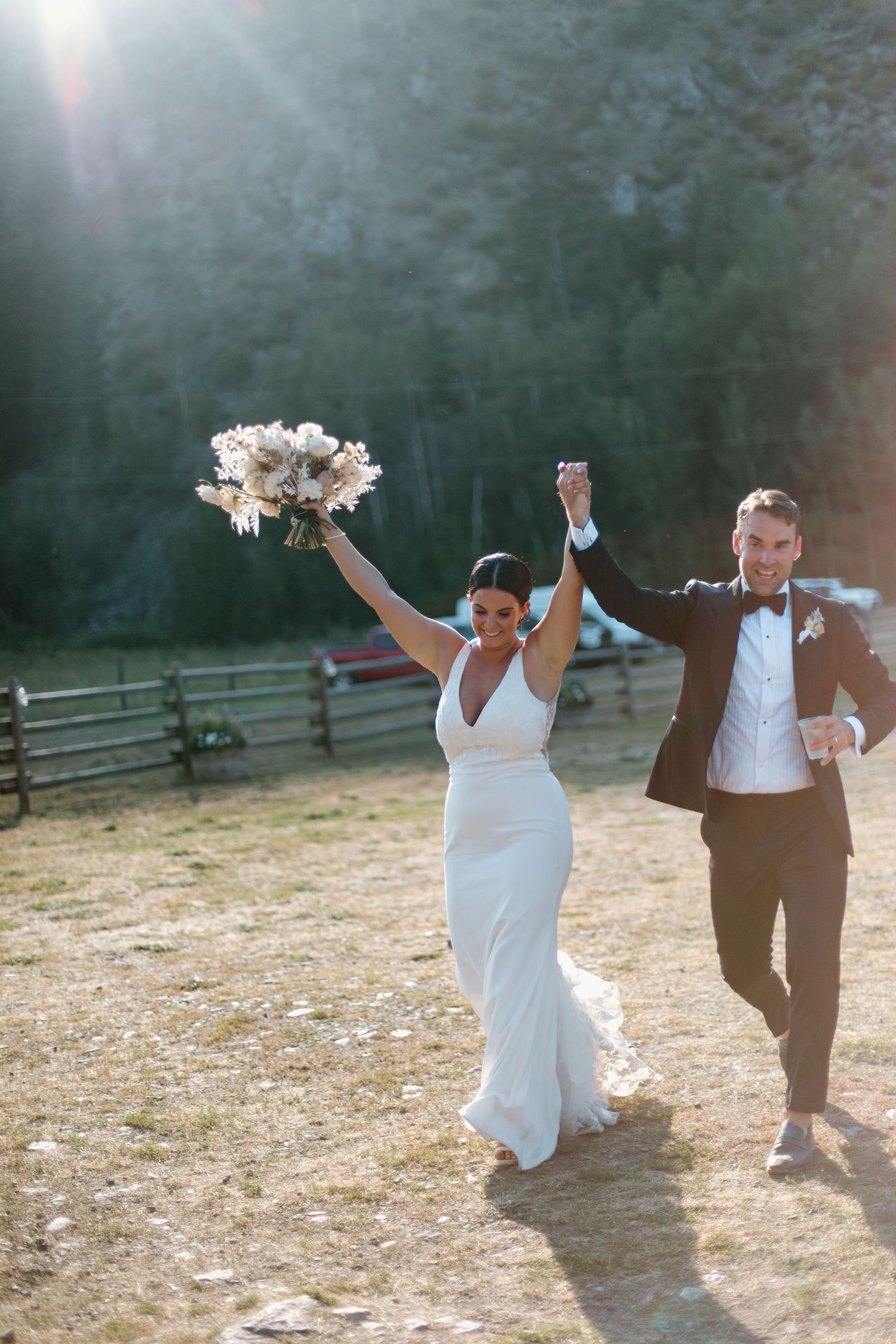 A joyful couple celebrates on their wedding day, raising their arms in celebration outdoors.