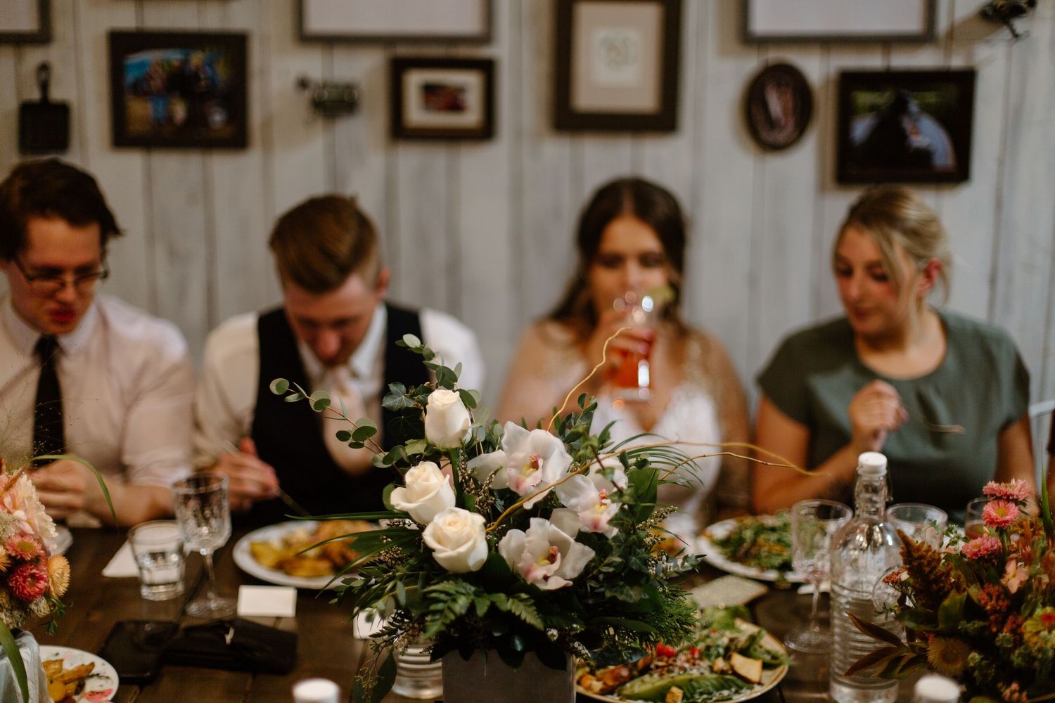 Wedding reception dinner table with floral centerpiece and dining guests.