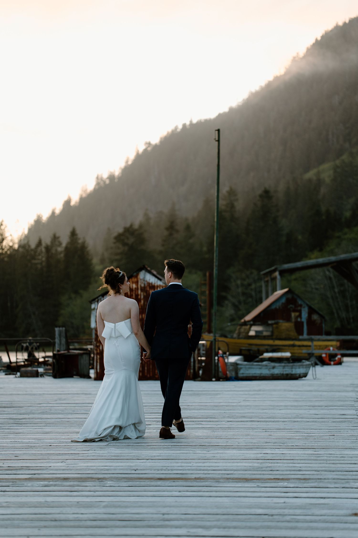 Couple walking on wooden dock with mountain landscape at sunset.