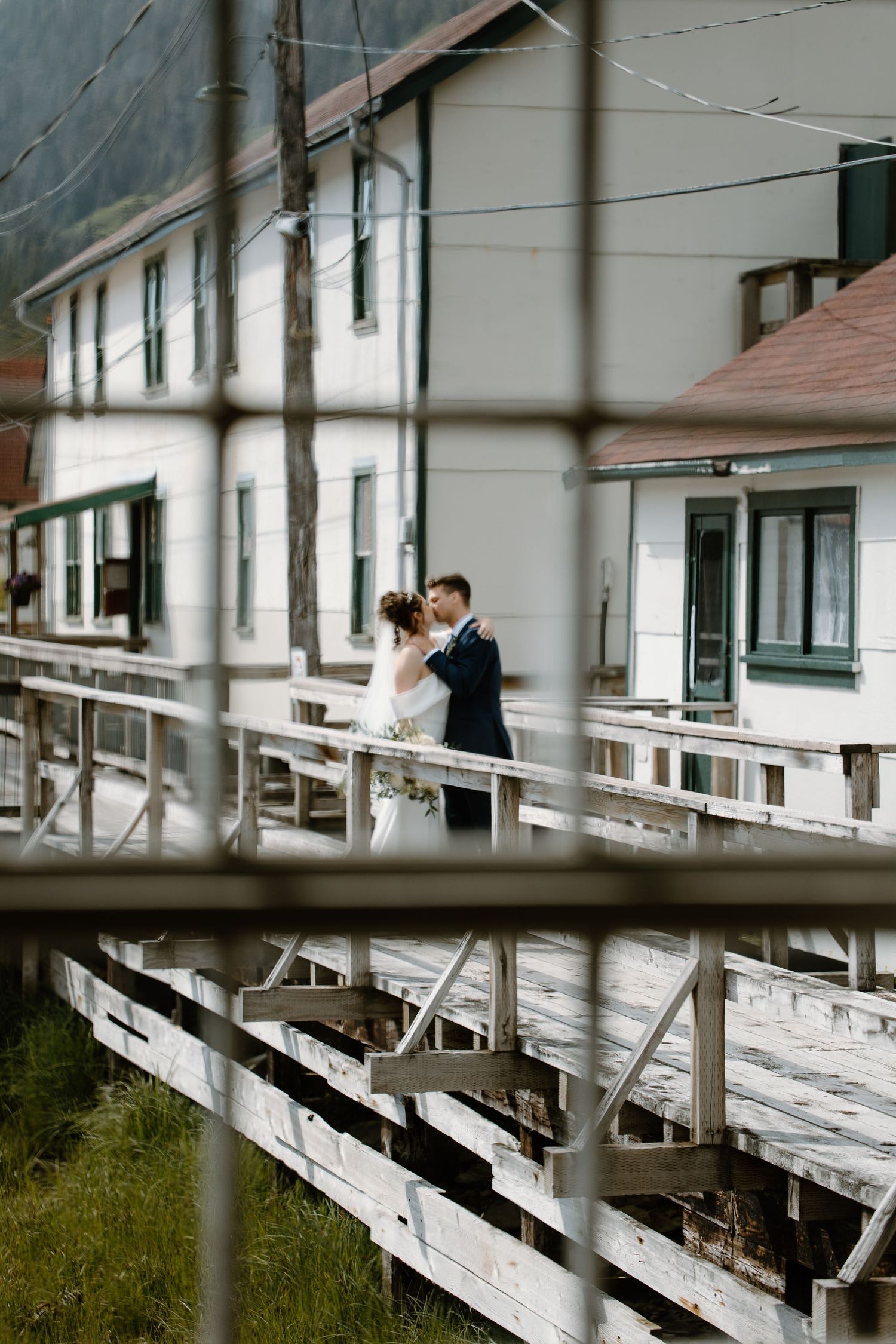 A romantic moment shared on a white wooden deck overlooking a scenic landscape at sunset.
