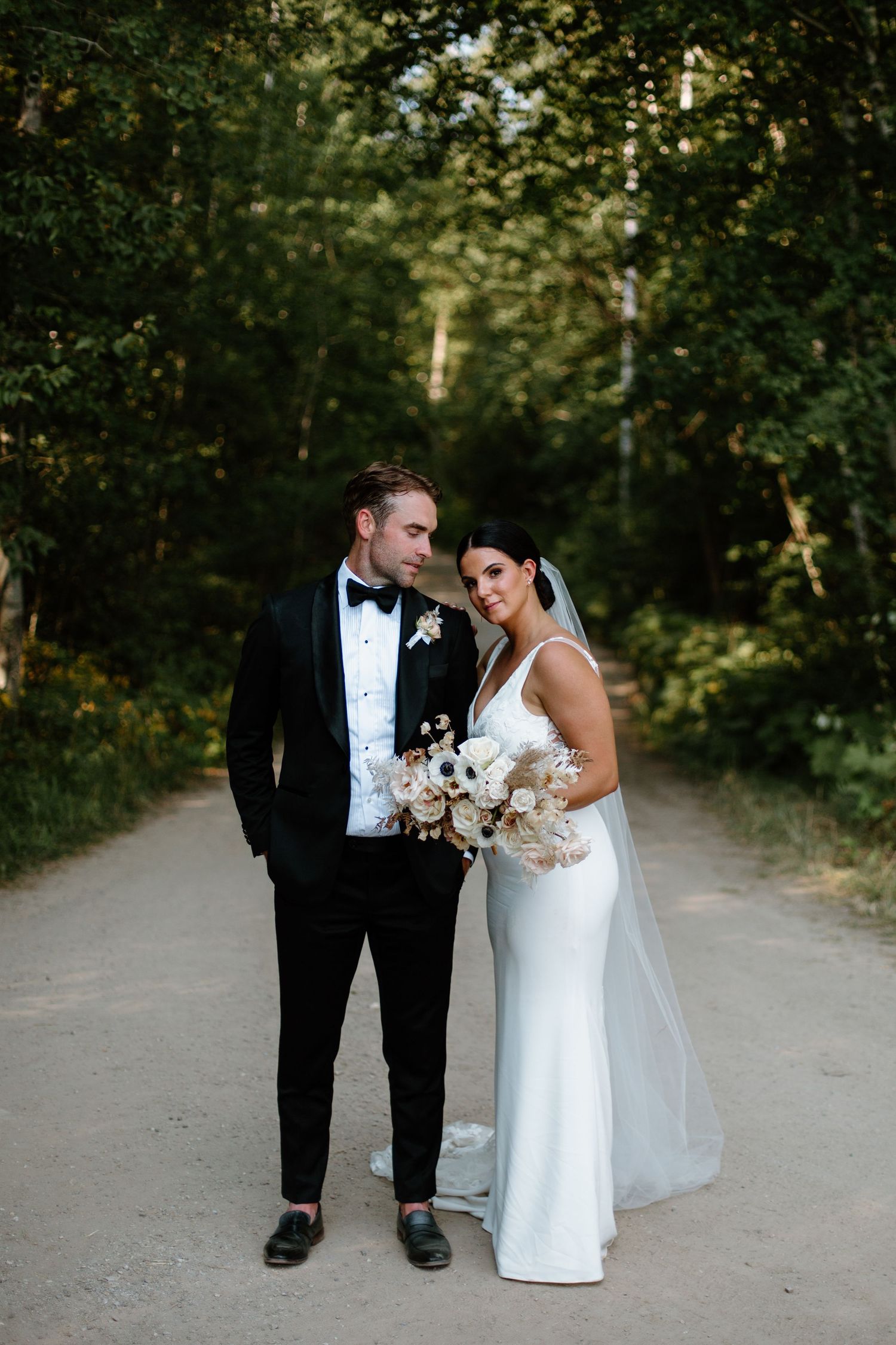 Wedding couple walking together on a tree-lined path in formal attire.