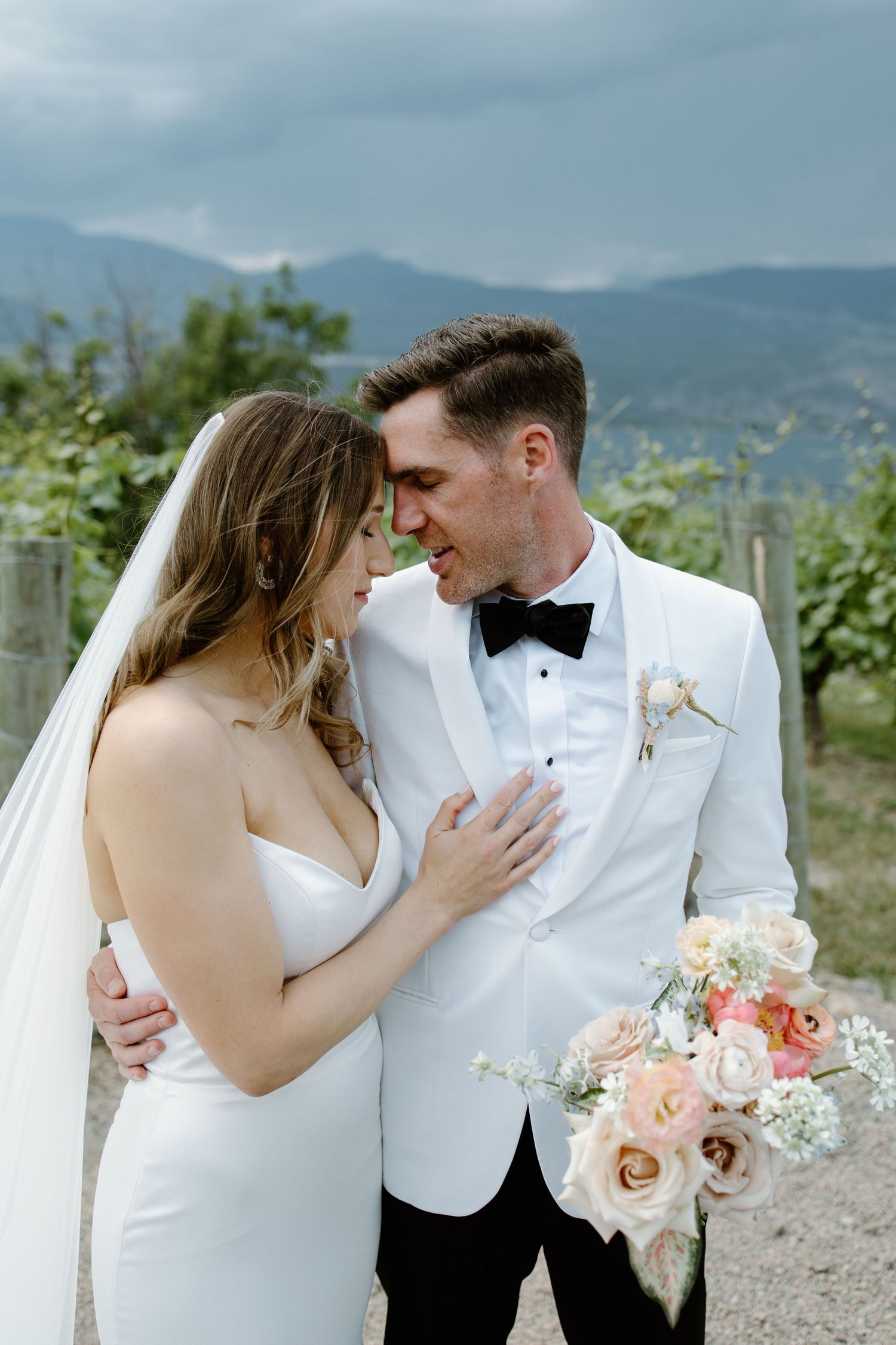 Elegant couple shares intimate moments in white attire against mountain backdrop.
