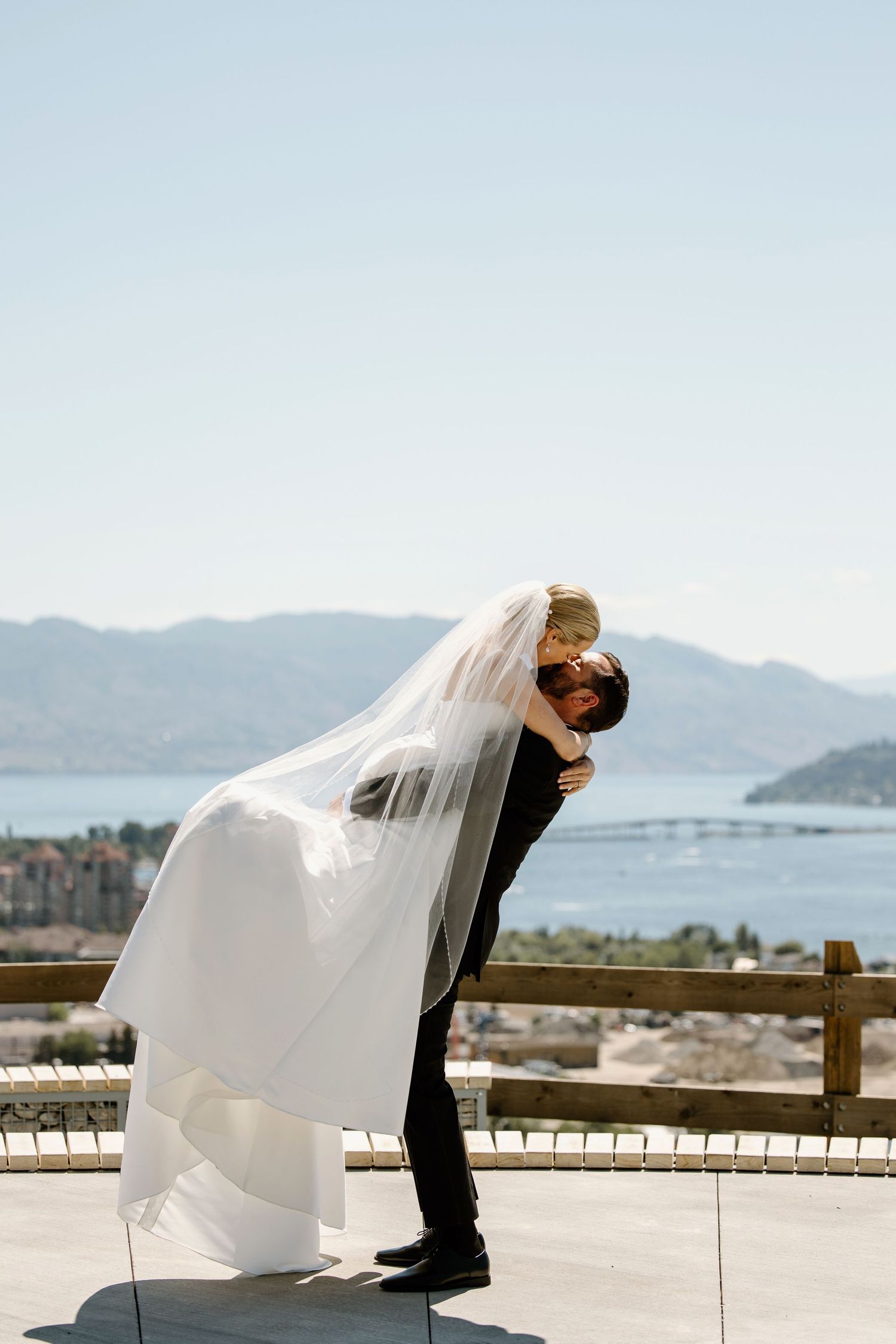 Dramatic wedding portrait with flowing veil against mountain and water backdrop.