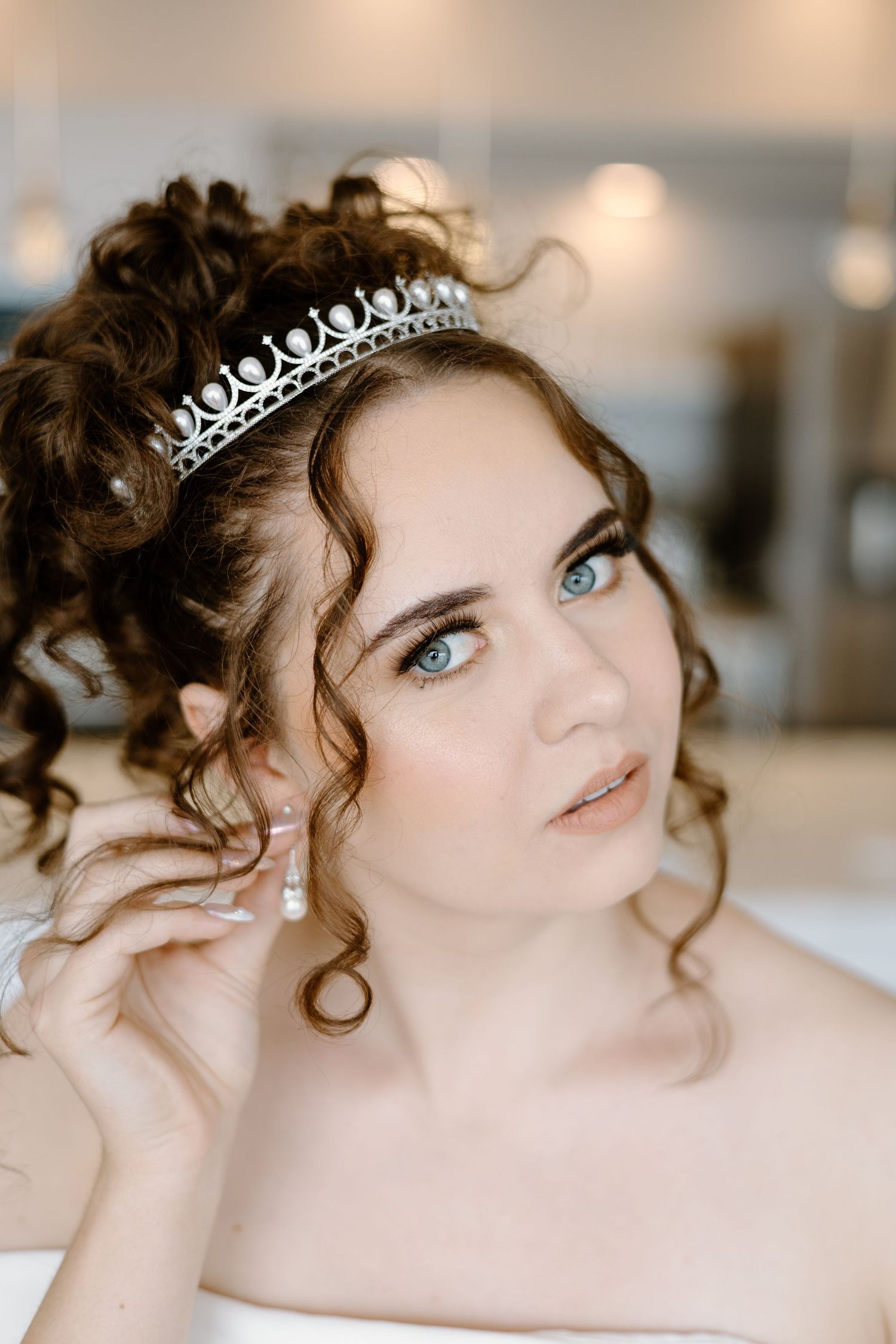 Delicate silver tiara adorns curled hair in soft bridal portrait.