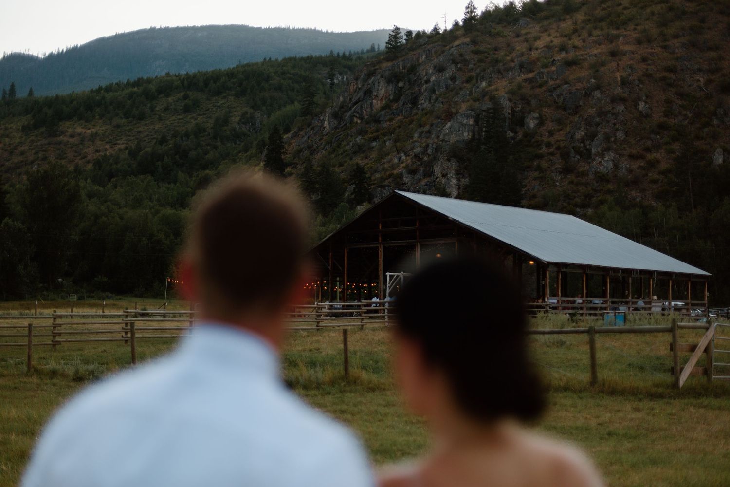 A rustic barn venue nestled against a mountainous landscape at dusk.