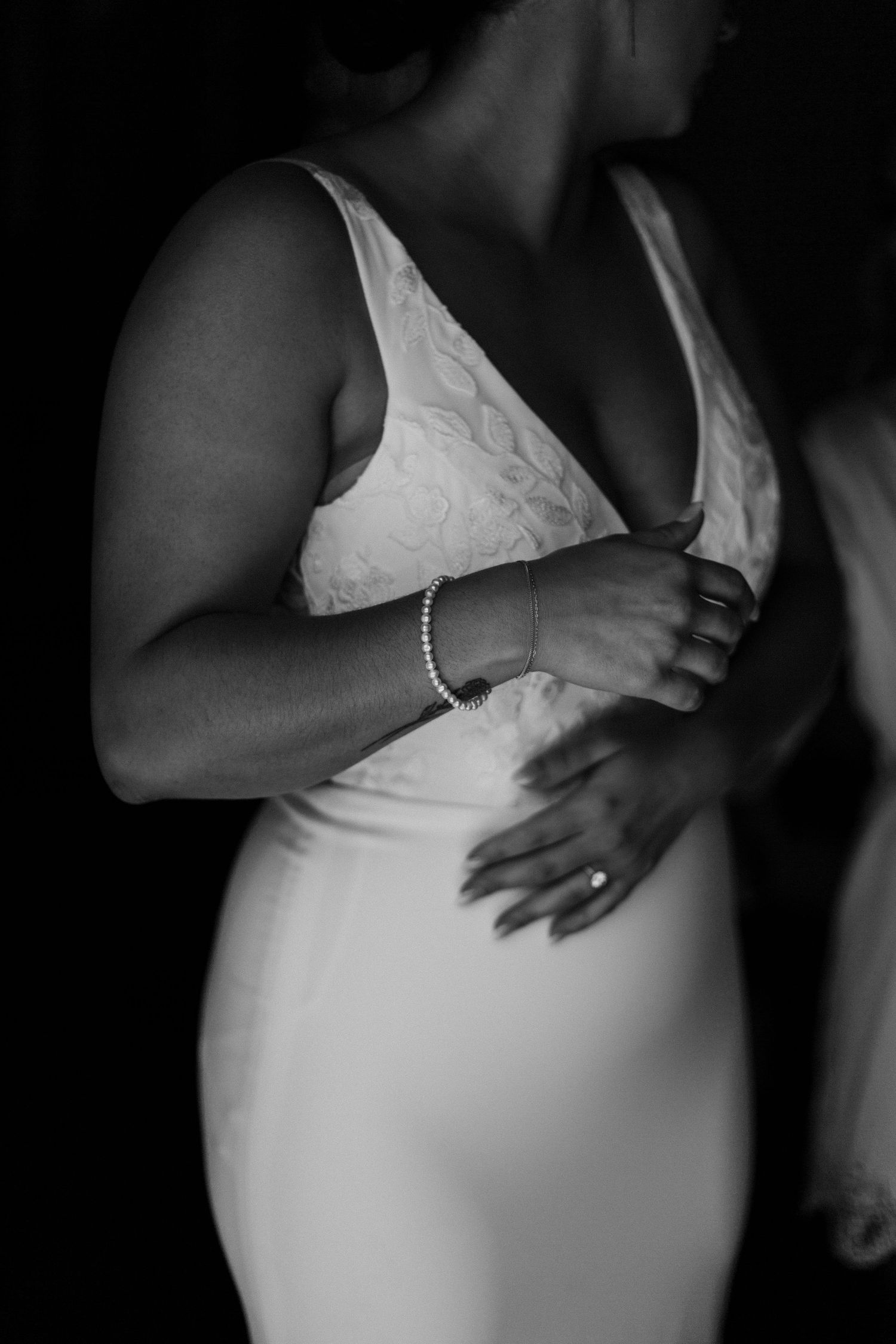 Elegant details of a fitted white lace wedding dress with pearl bracelet in black and white.