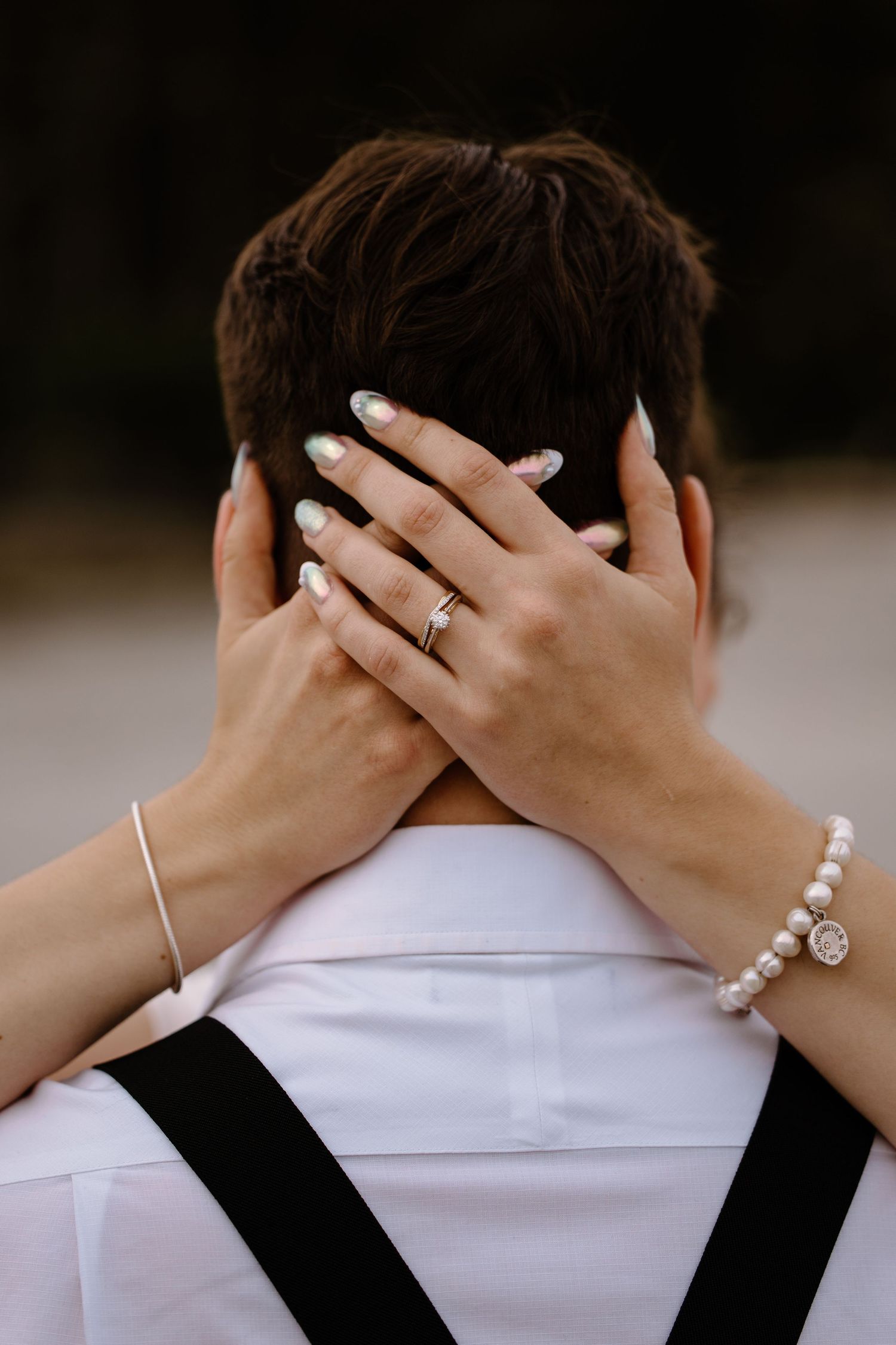 Hands wearing jewelry and bracelets embrace from behind in an intimate moment.