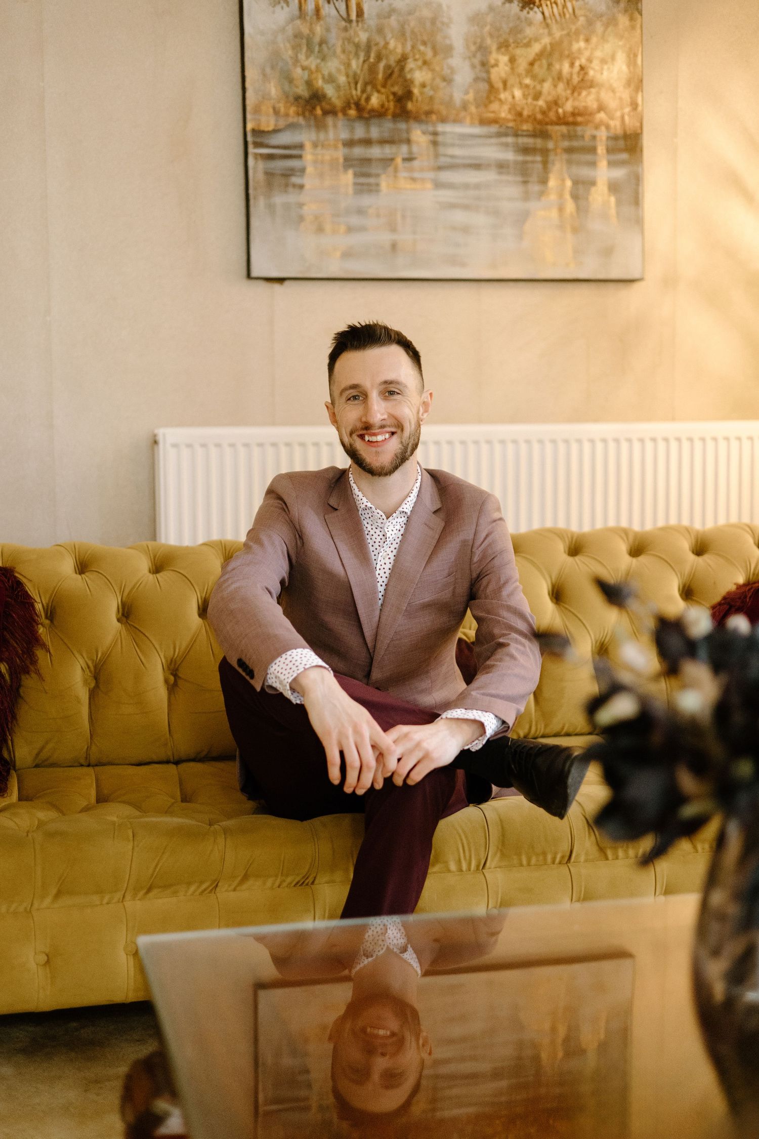 Casual business portrait on a yellow tufted sofa with natural lighting and modern decor.