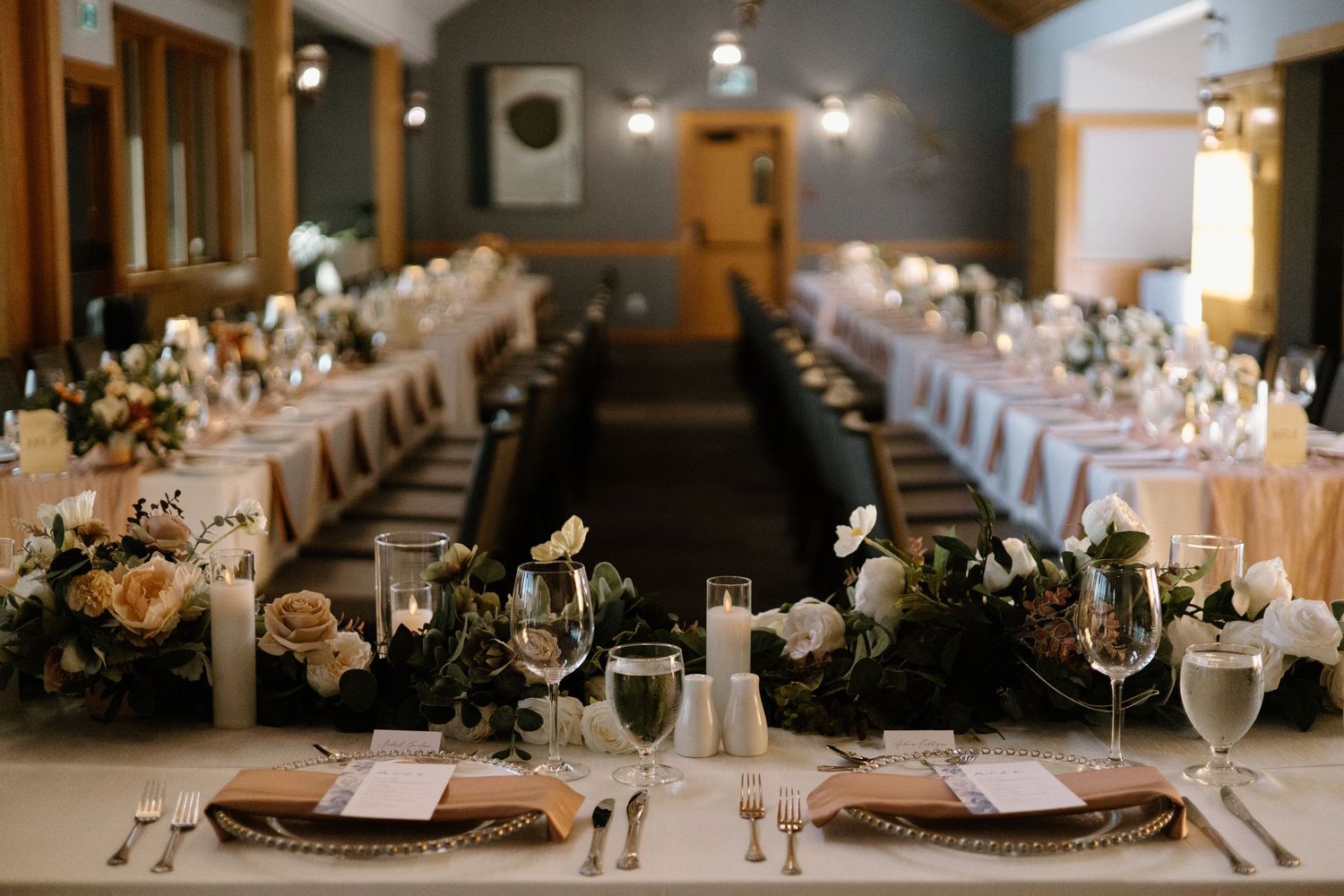 Elegant wedding reception table setup with long rows of place settings and romantic lighting.