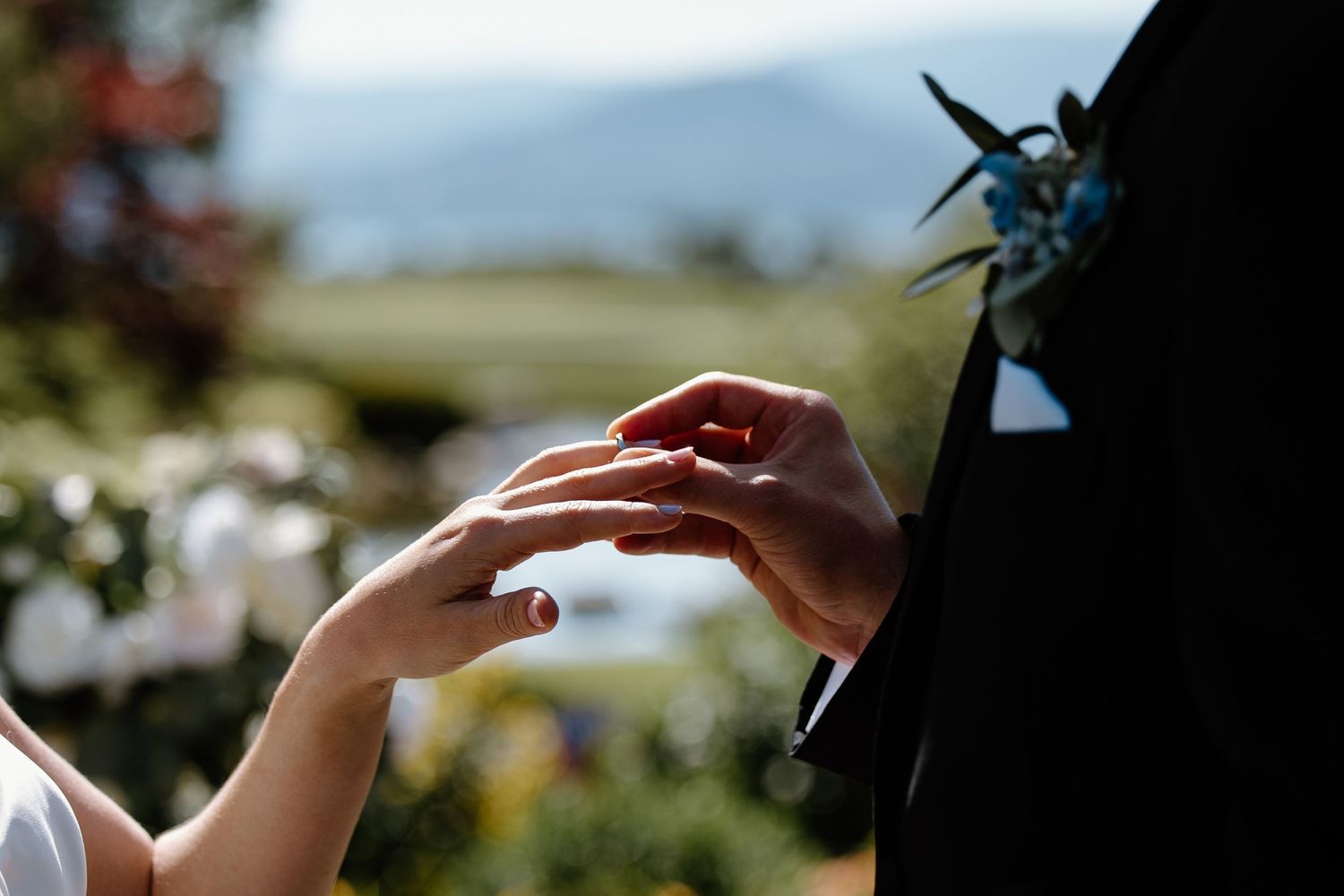 Close-up of hands exchanging rings during an outdoor wedding ceremony.
