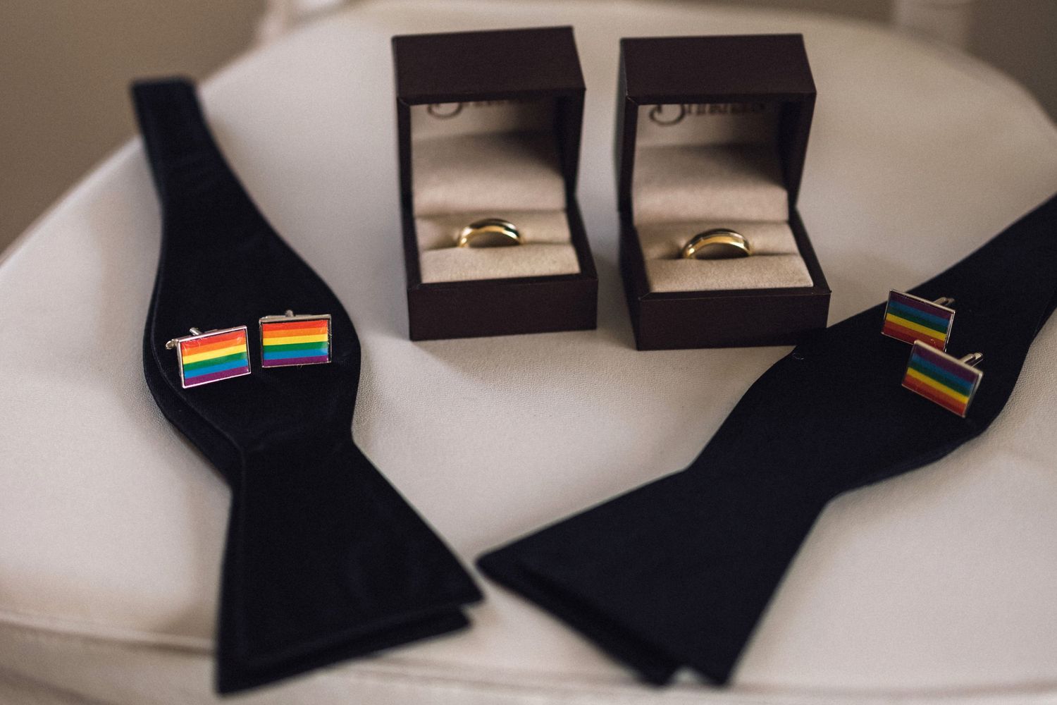 Wedding accessories including rainbow pride bow ties and wedding rings in black boxes.