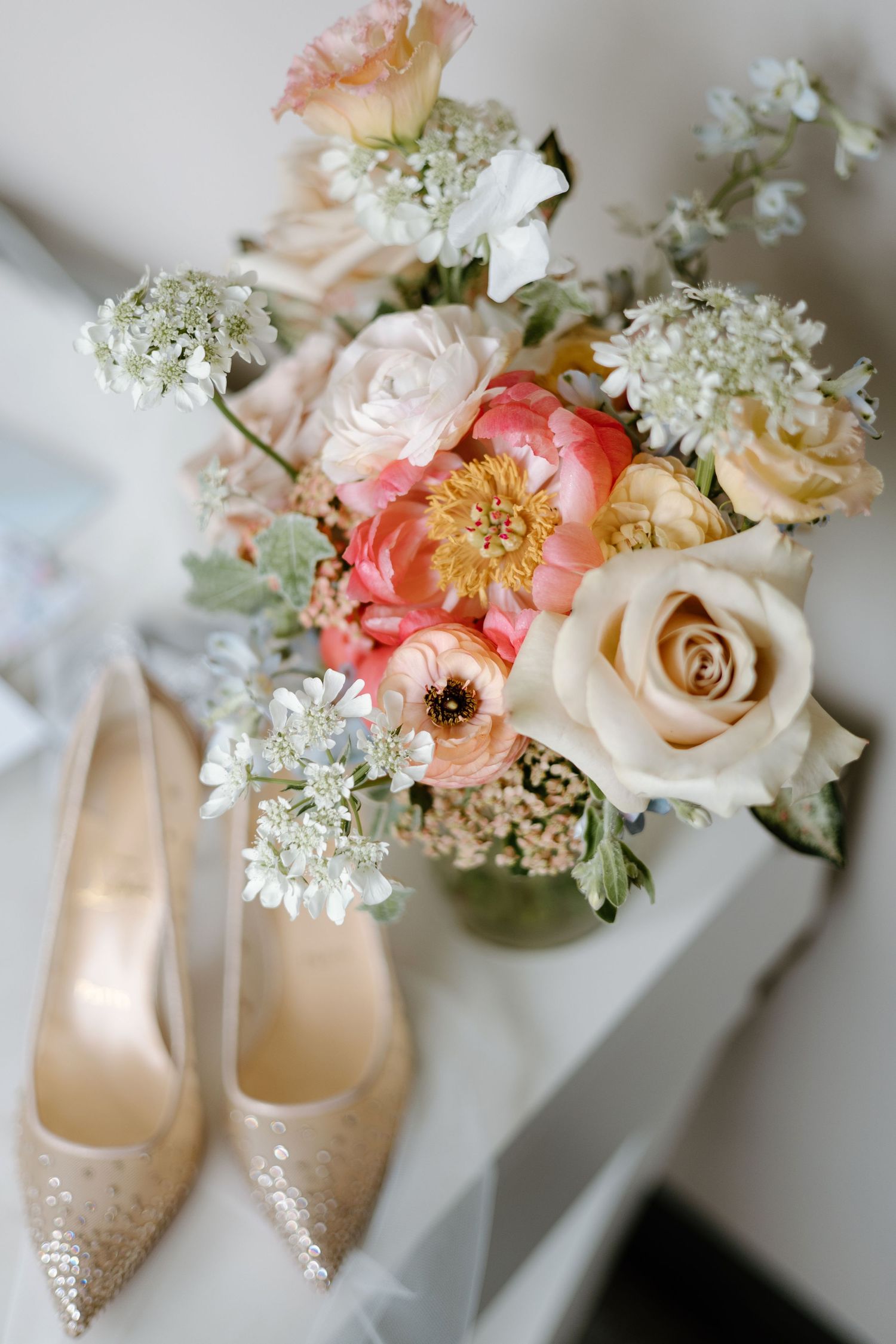 Elegant bridal details featuring sparkly heels and a soft peach and white floral arrangement.