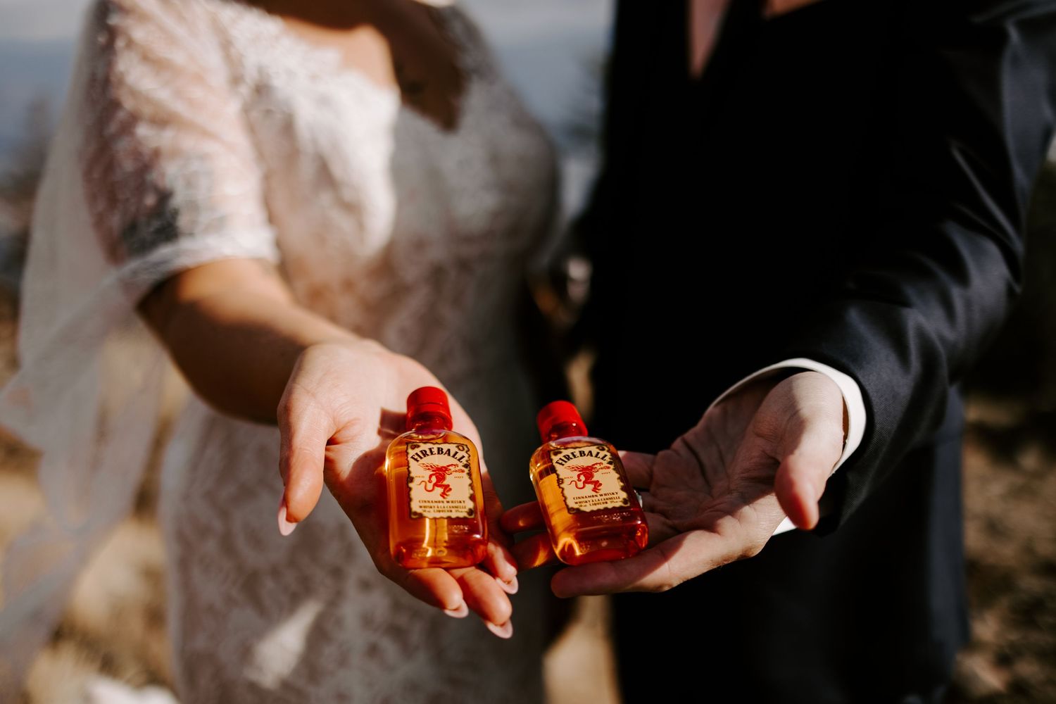 Close-up shot of hands holding amber-colored drinks in crystal glasses during an outdoor celebration.