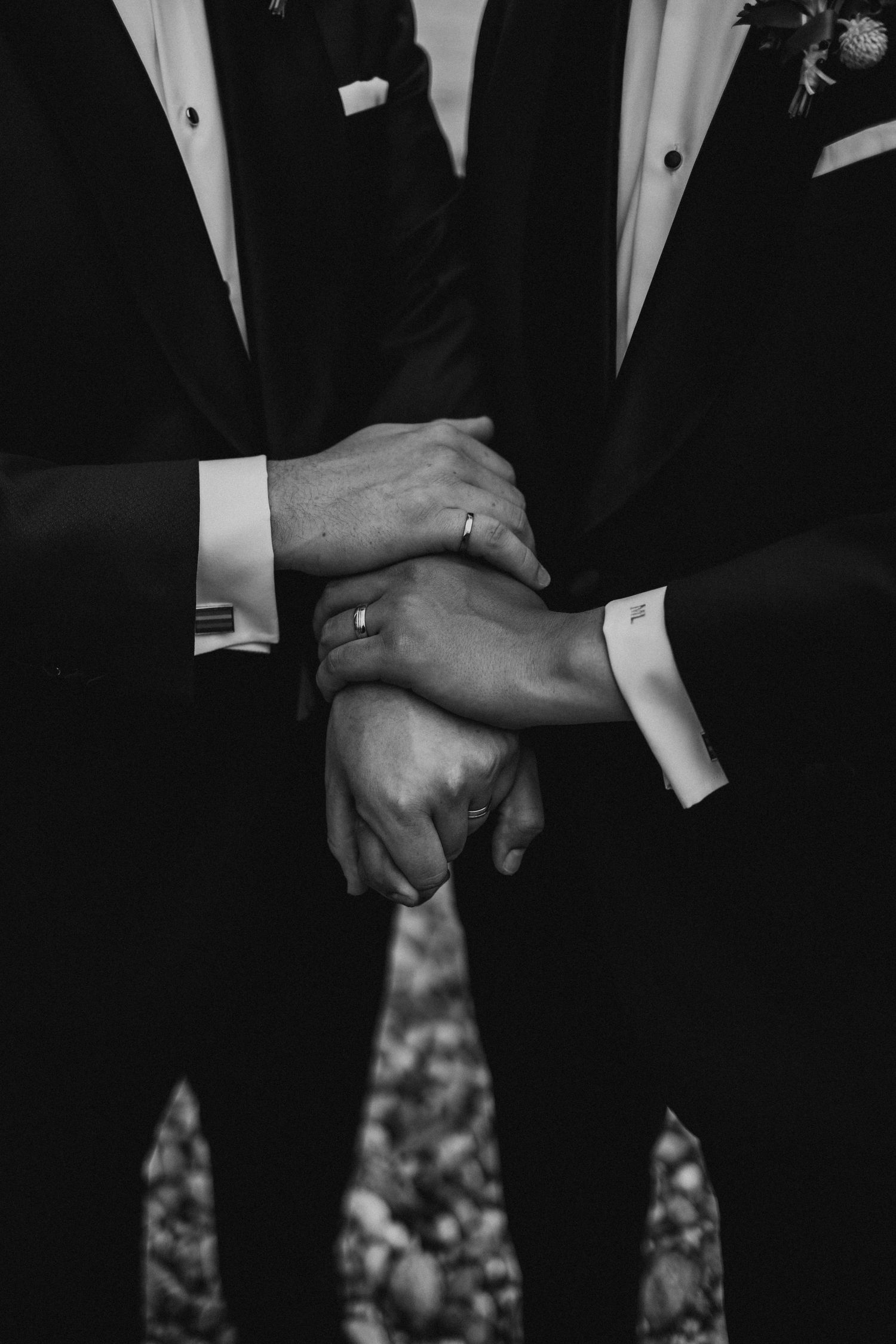 Black and white close-up photograph showing multiple hands of people wearing formal suits and dress attire.