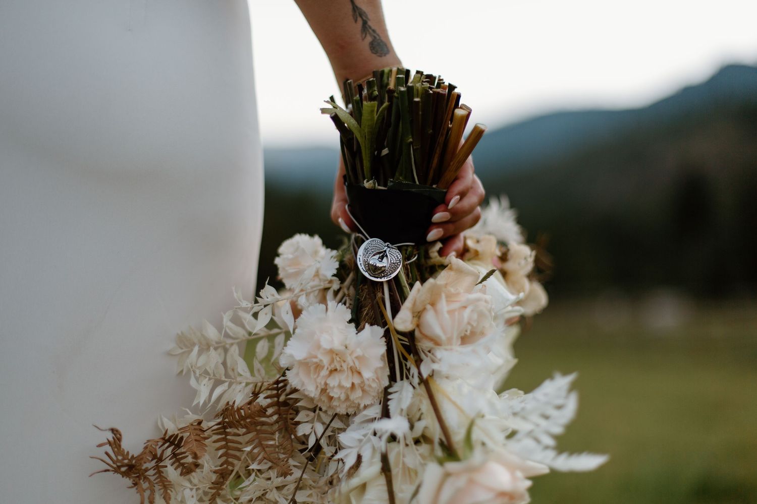 Close-up of a wedding bouquet featuring white flowers and dried elements against a mountain backdrop.