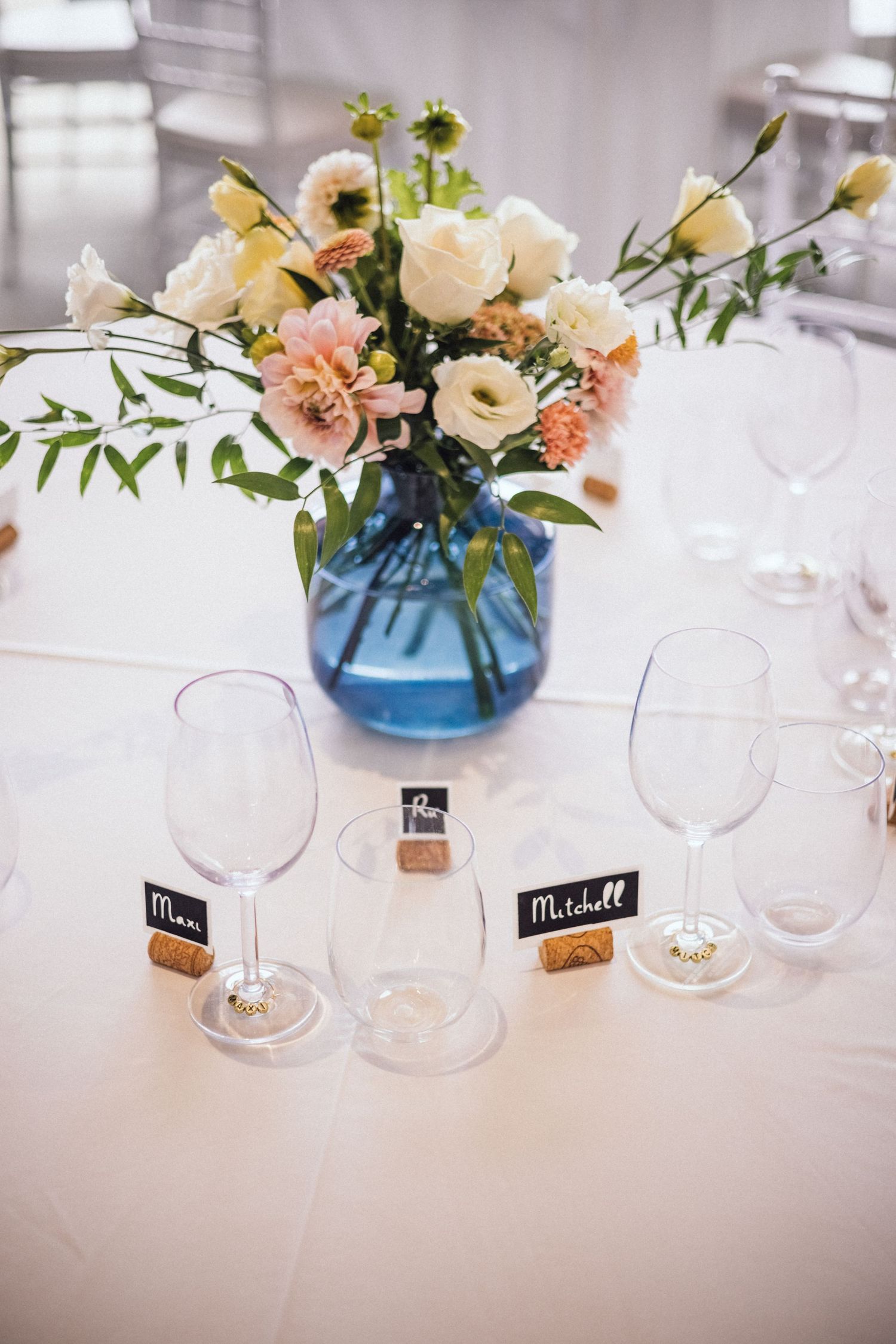 Wedding table centerpiece with pink and white flowers in a blue vase next to wine glasses.