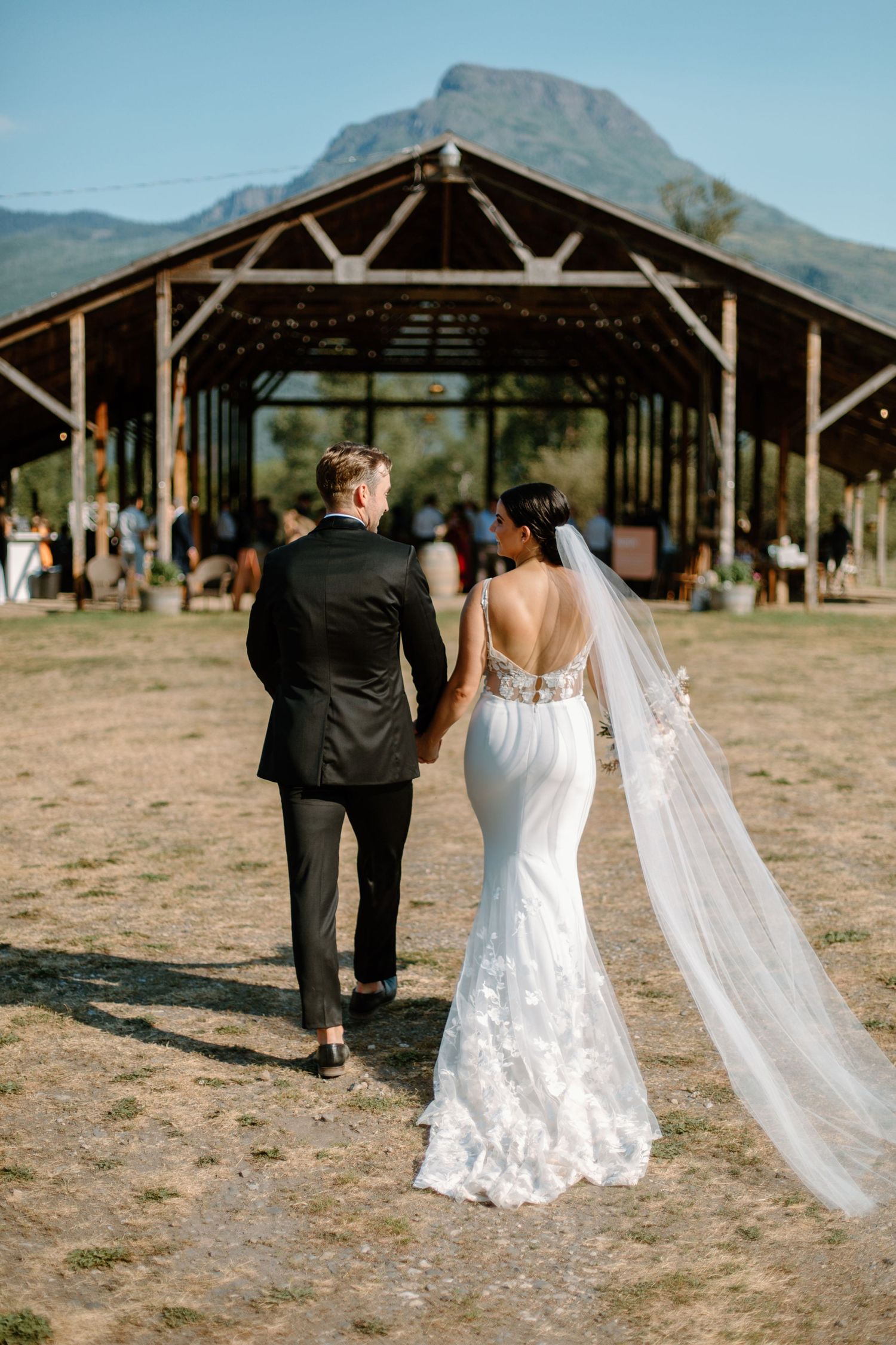 A wedding couple walks across a desert landscape with mountains in the background on their special day.