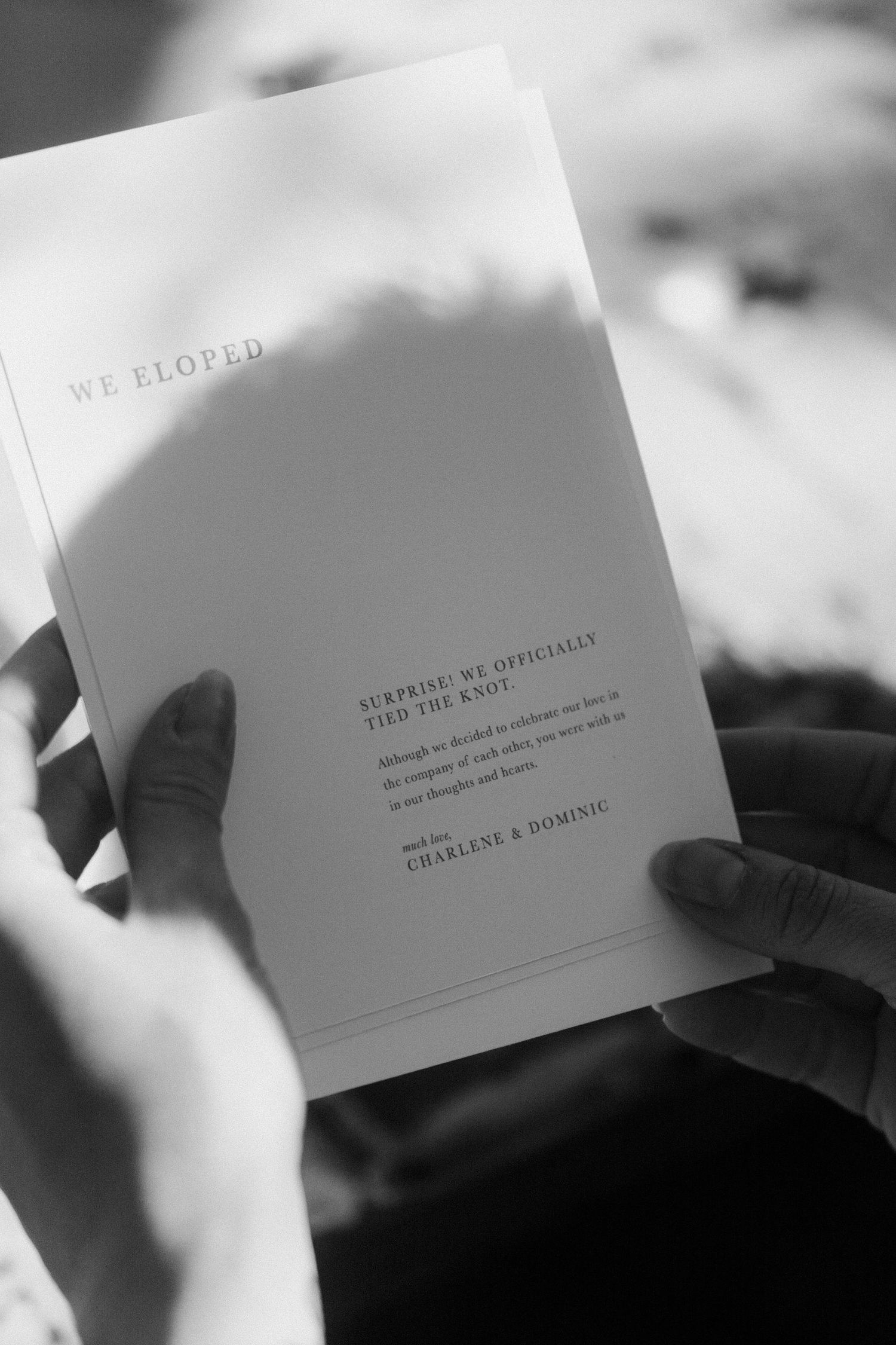 Black and white close-up of minimalist wedding invitation being held in hands.