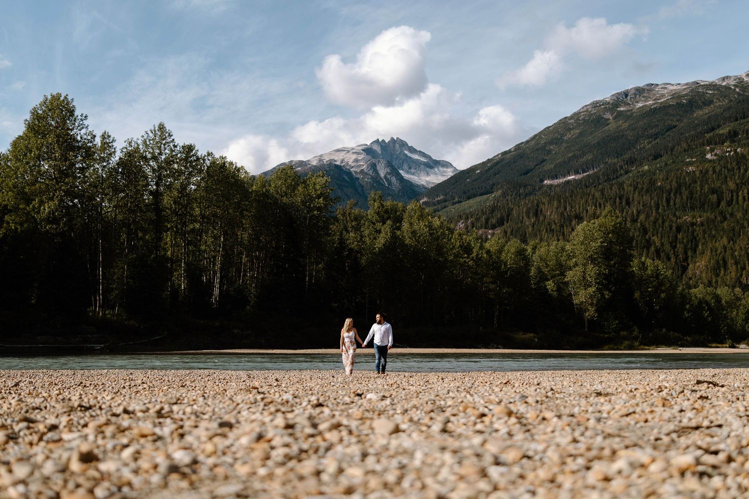 Scenic mountain landscape with a couple walking in the distance on a rocky beach.