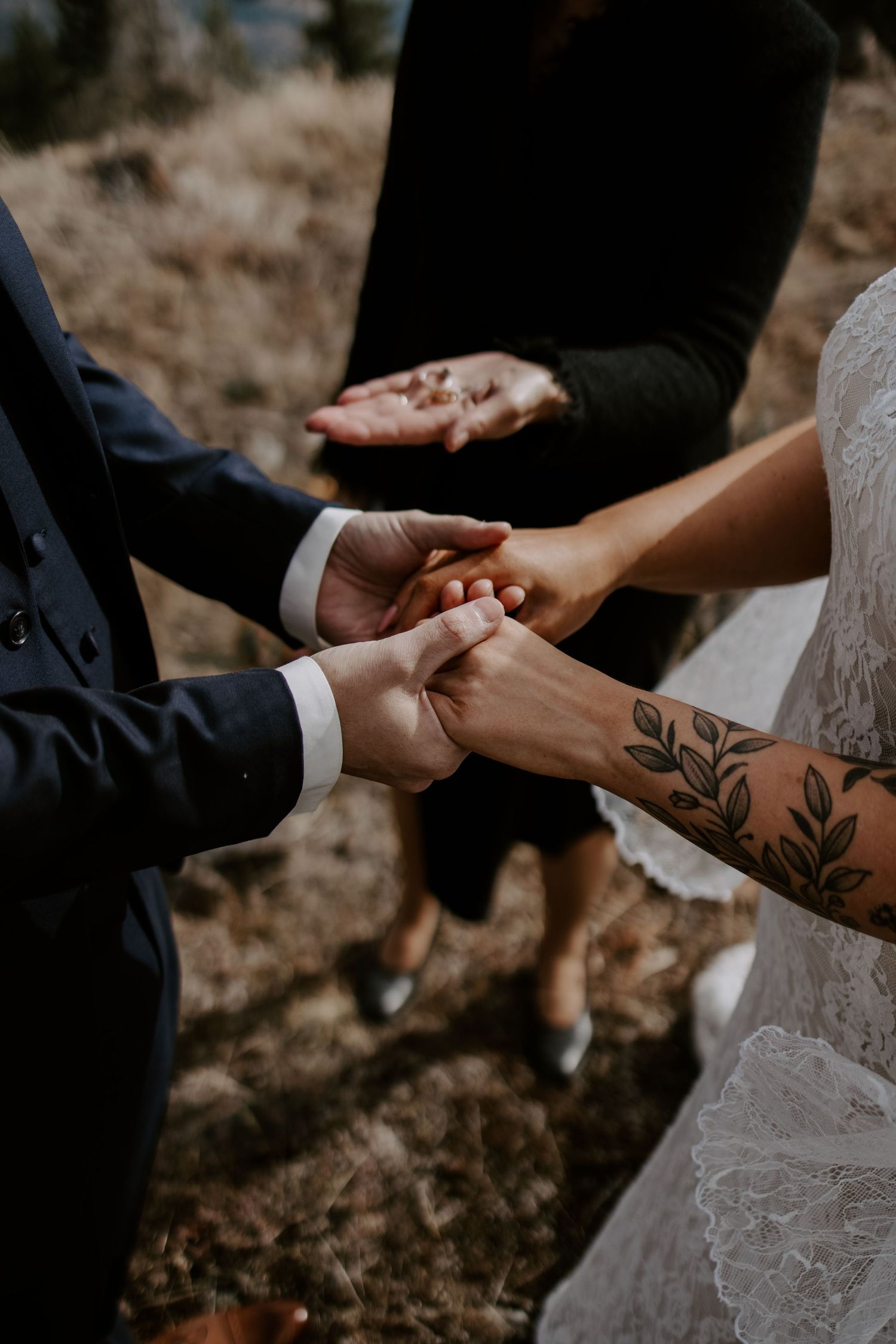 Close-up of hands exchanging rings during a wedding ceremony with visible floral tattoos.