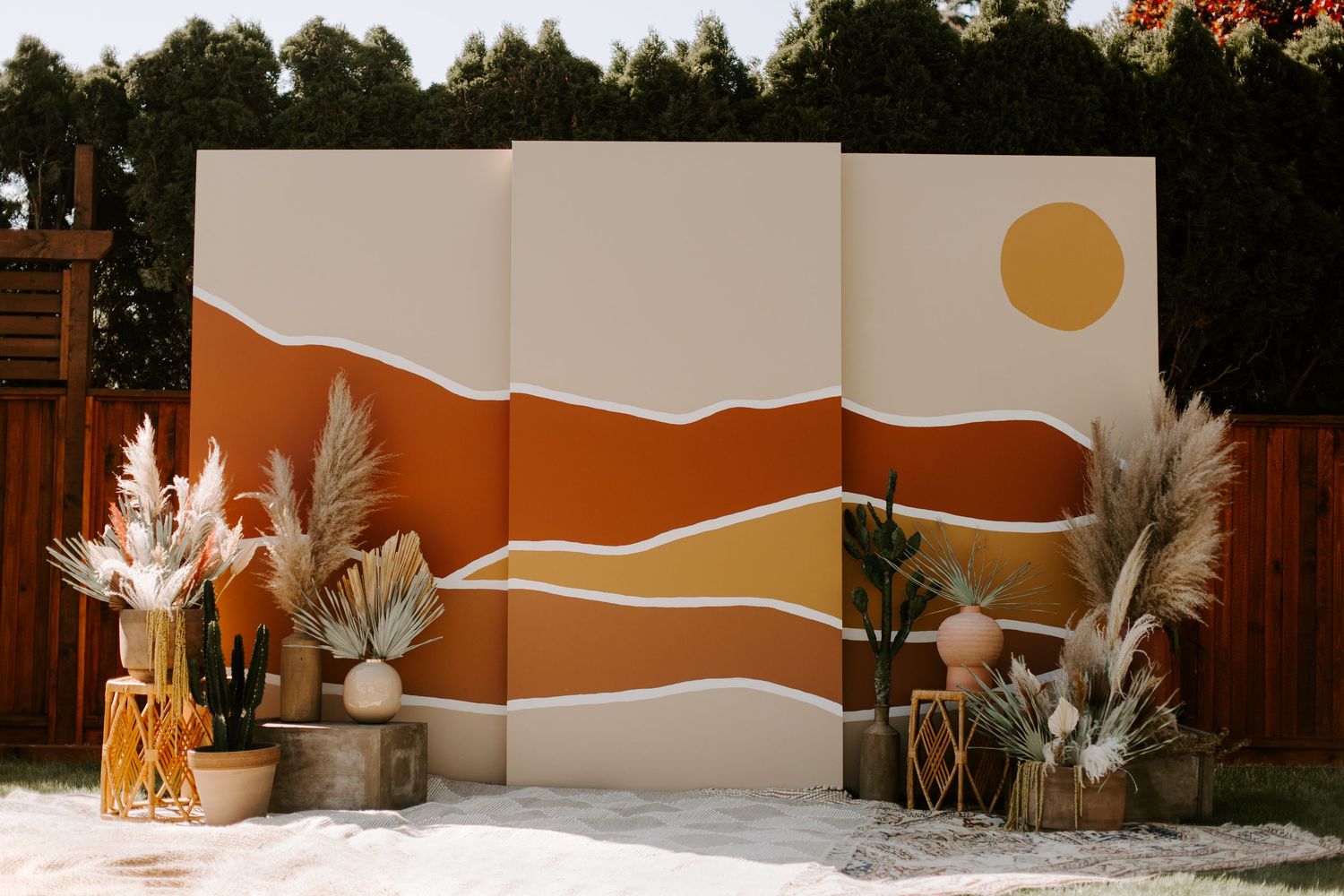 Modern desert-themed wedding backdrop with orange and white waves and pampas grass decor.