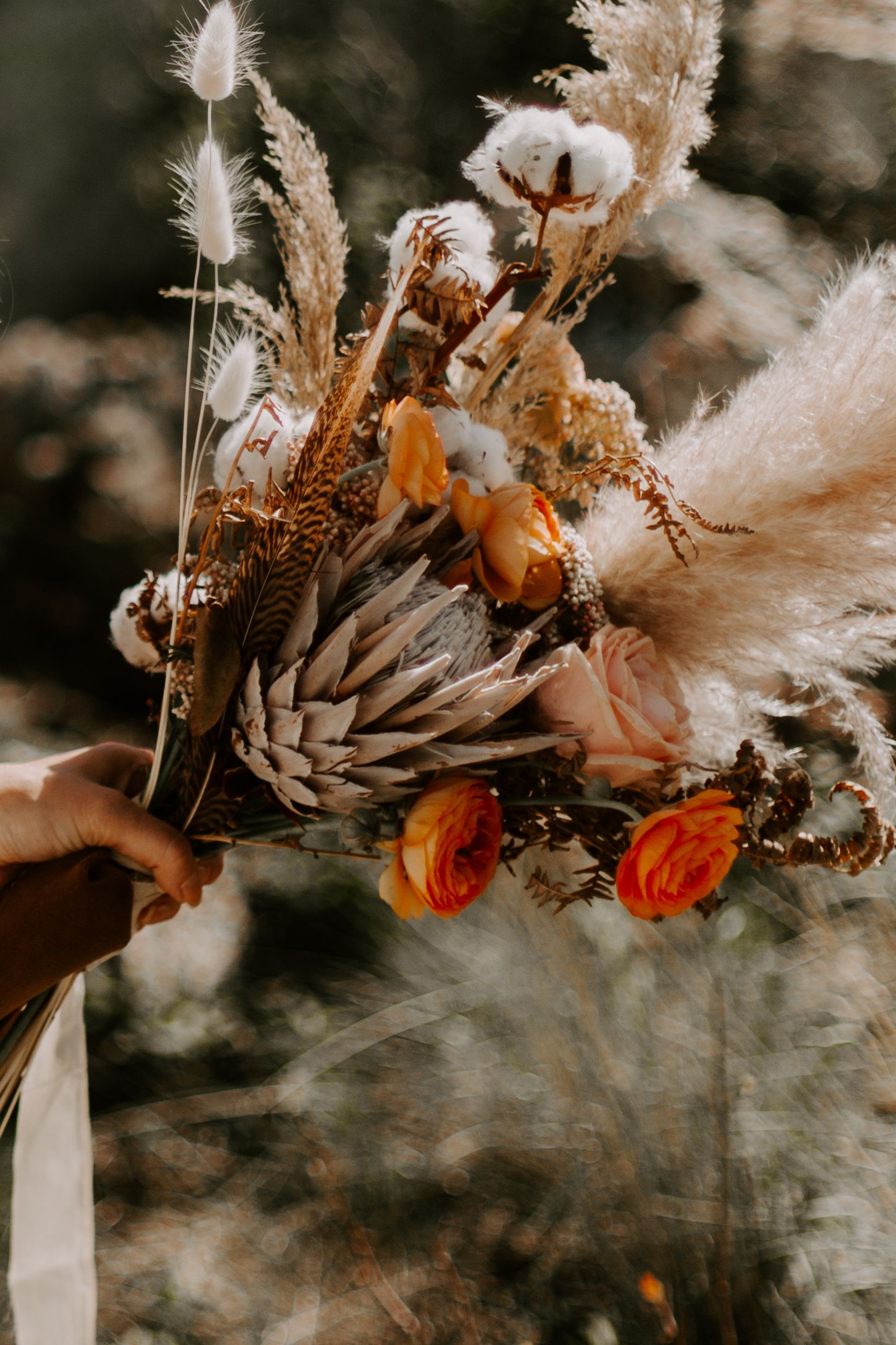 Dried floral arrangement featuring pampas grass and autumn-colored elements in a white vase against a dark background.