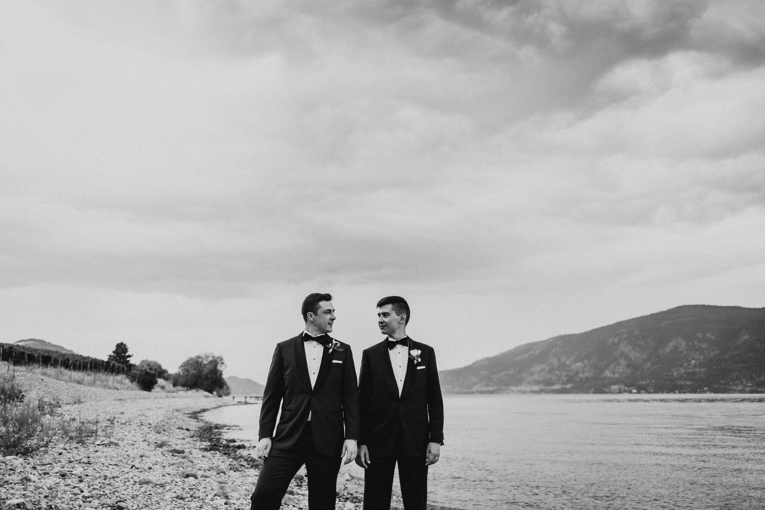 Two people in formal attire stand together against a scenic mountain landscape.