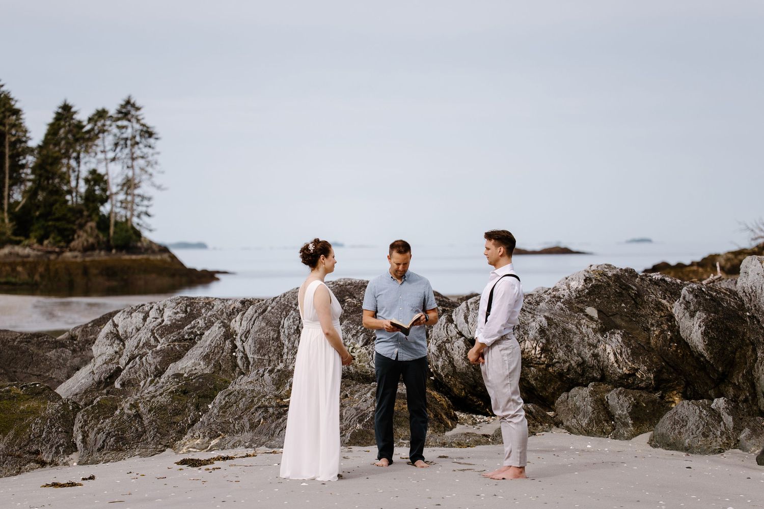 A coastal wedding ceremony takes place on rugged rocky cliffs overlooking the ocean at sunset.