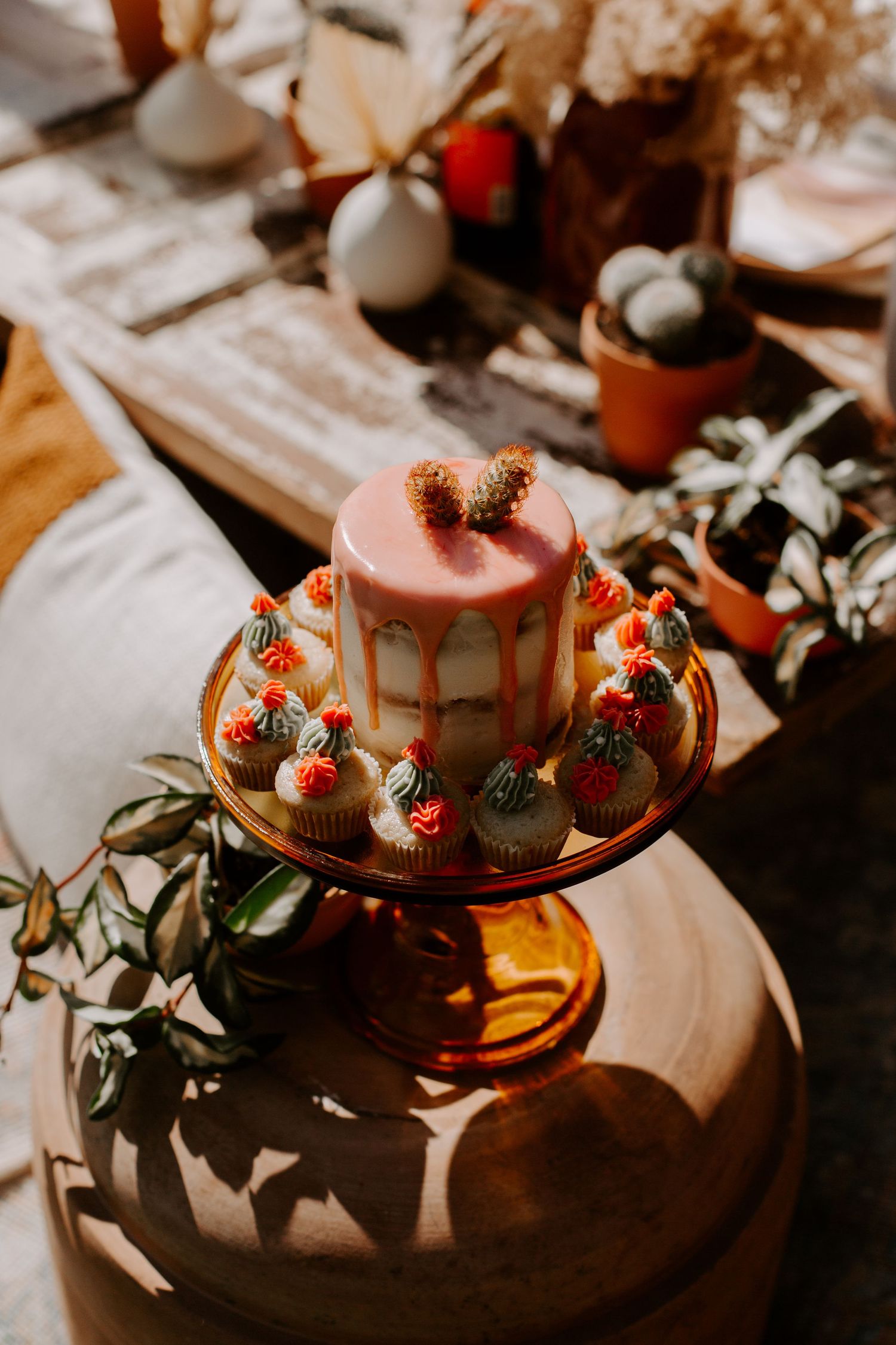 Pink frosted cake decorated with fresh strawberries and greenery on a wooden cake stand in moody lighting.